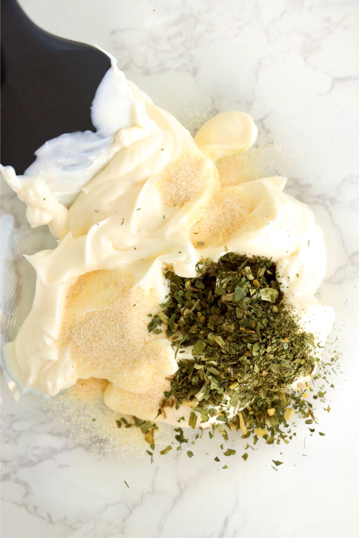 Mayonnaise and herbs combined in a mixing bowl.