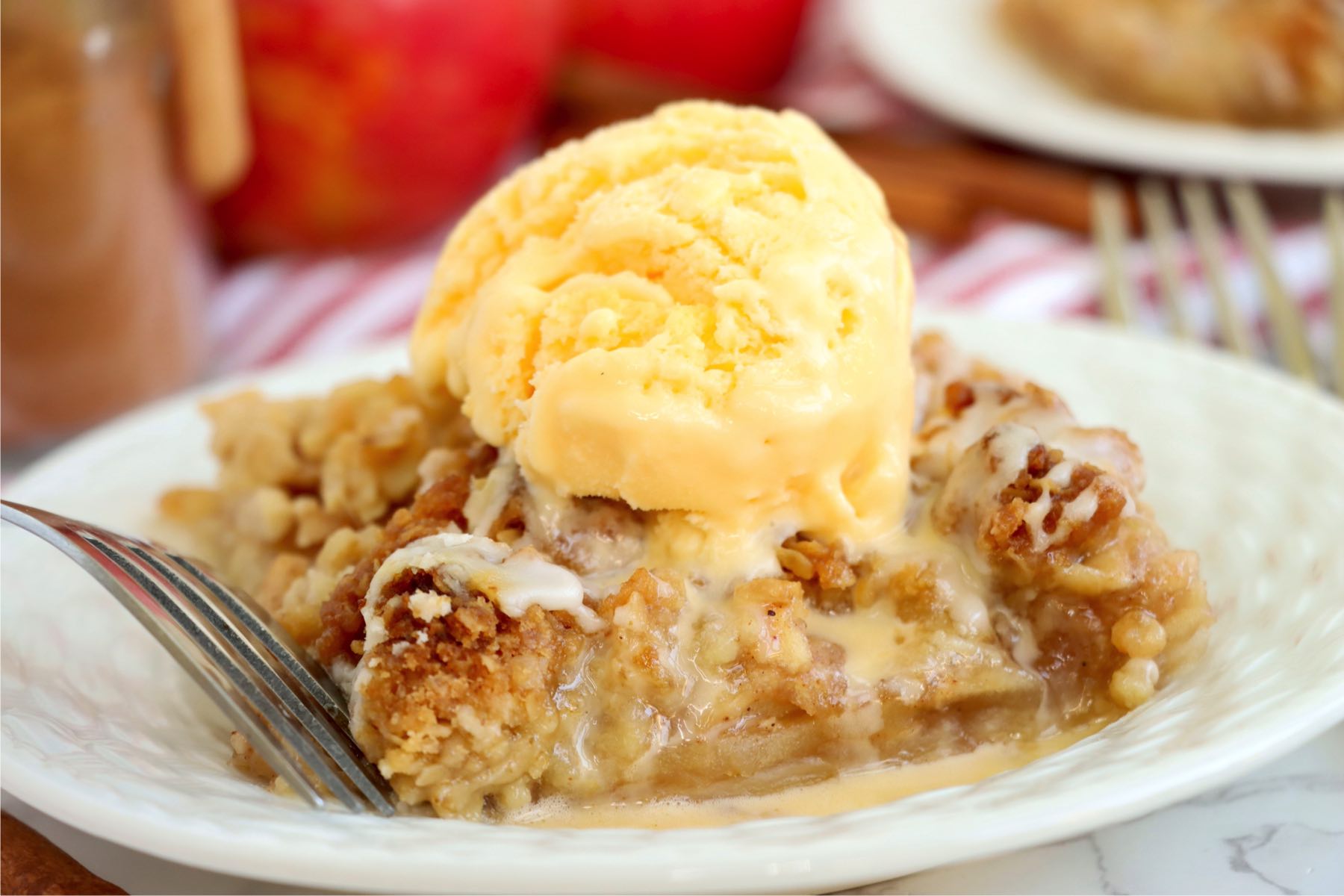 Piece of apple pie with ice cream on a white plate.