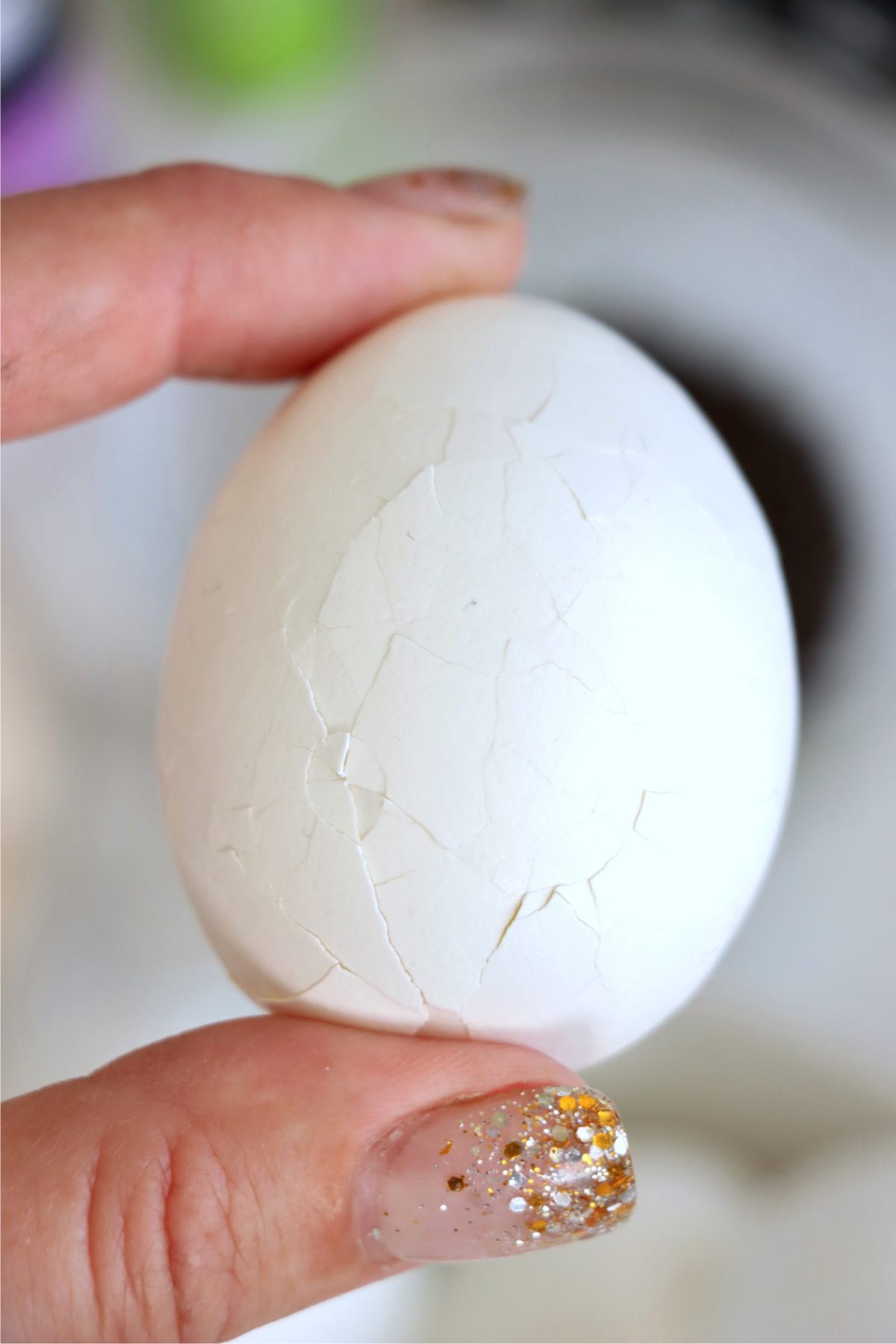 A cracked hardboiled egg held in between two fingers.