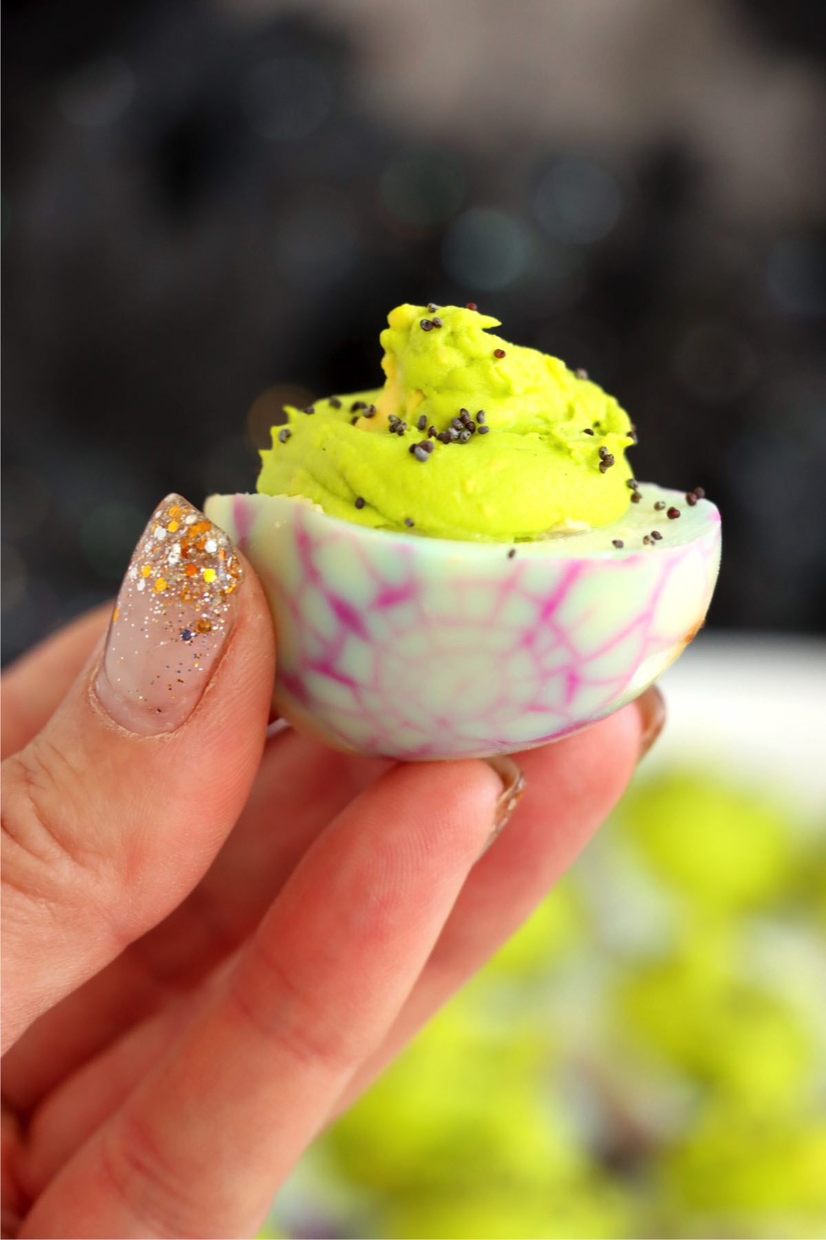 Fingers holding up a deviled egg filled with neon green filling for Halloween.