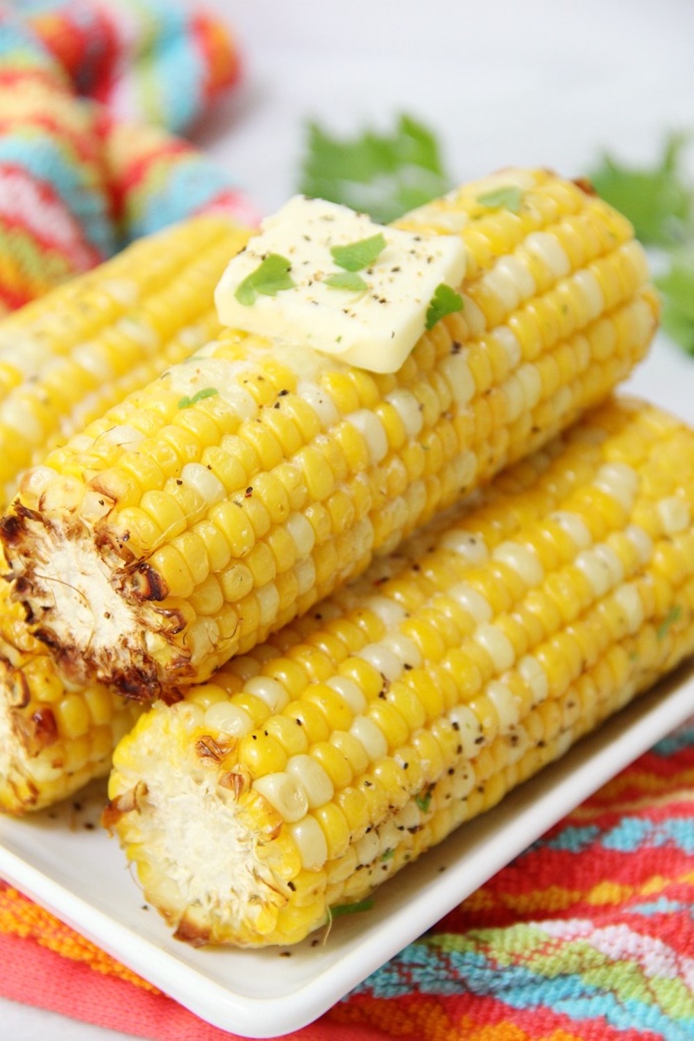 Air fryer corn on the cob on white serving dish with butter.