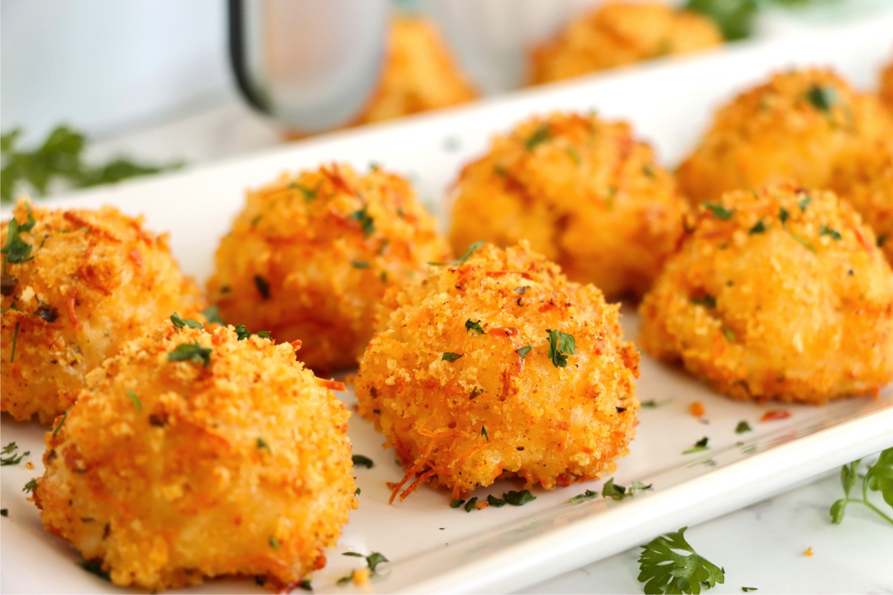 Mac and cheese filled balls on a white platter in front of an air fryer.