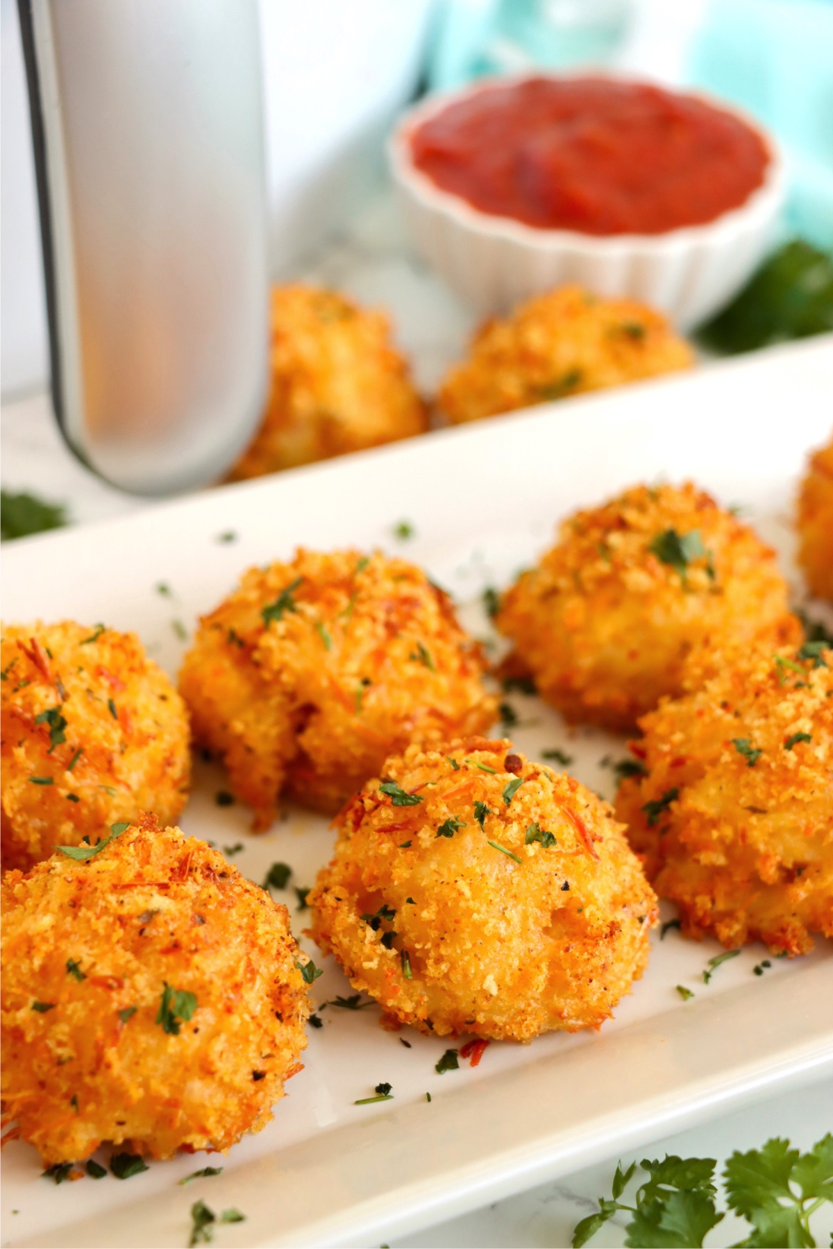 Platter filled with Panko-breaded mac and cheese bites in front of a silver air fryer.