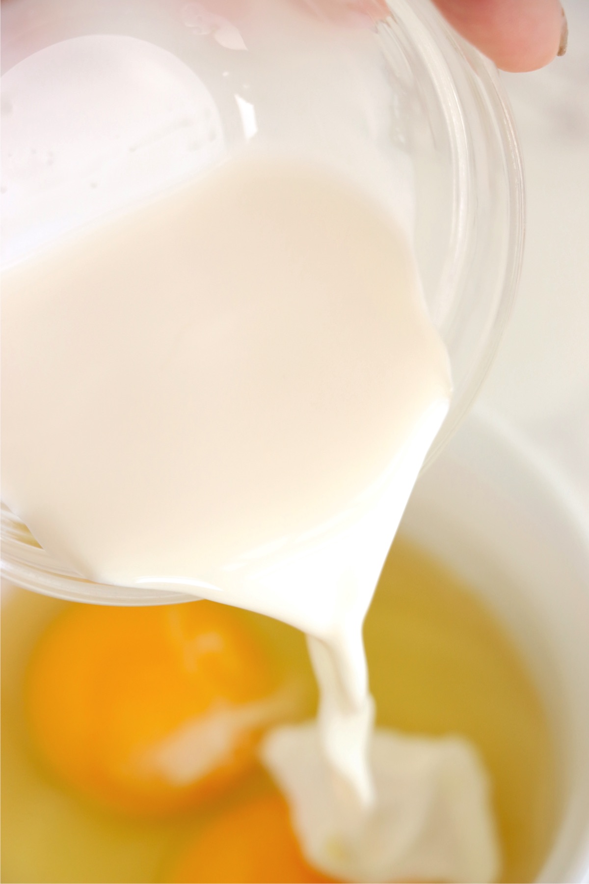 Pouring milk into a bowl filled with eggs.