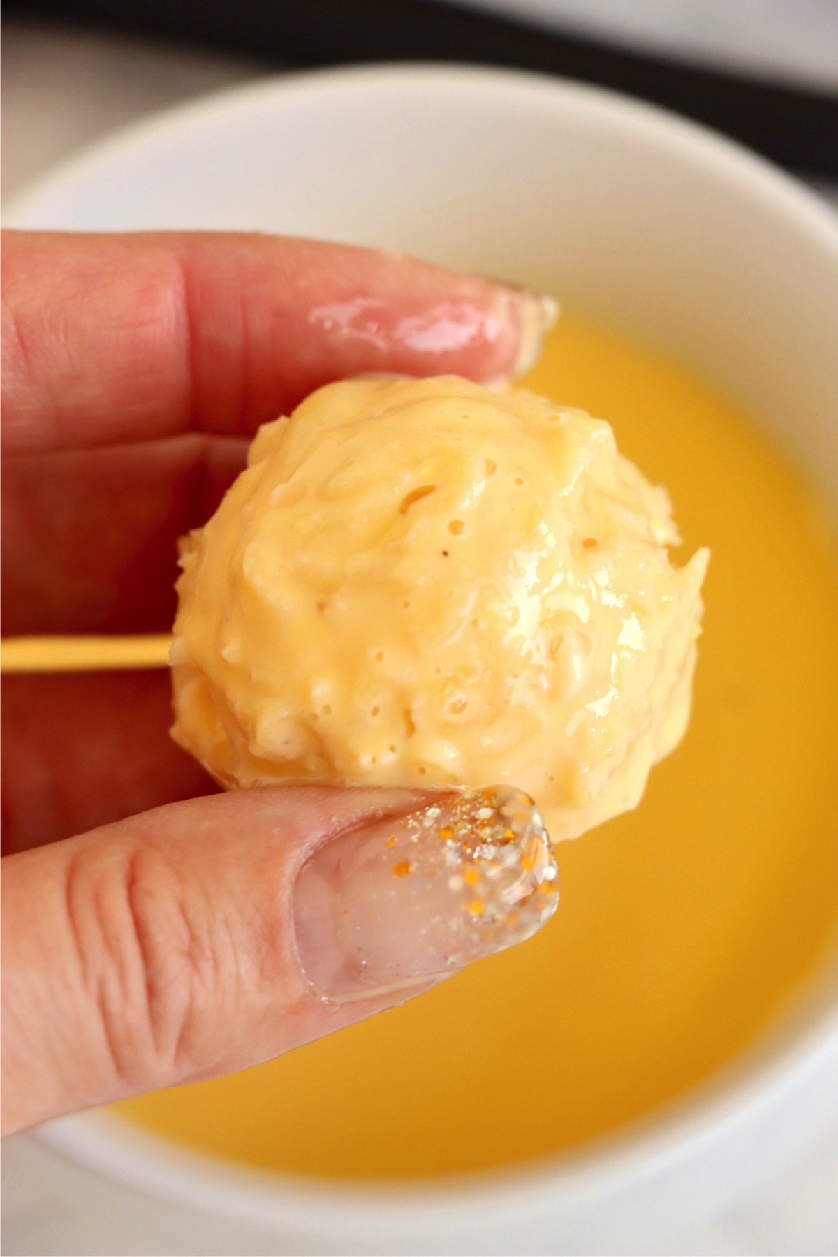 Fingers holding a mac and cheese ball dipped in an egg mixture.