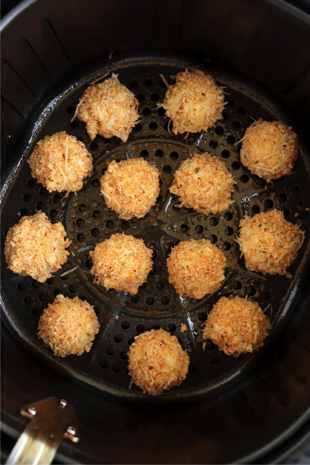 Breaded balls of mac and cheese in the basket of an air fryer.