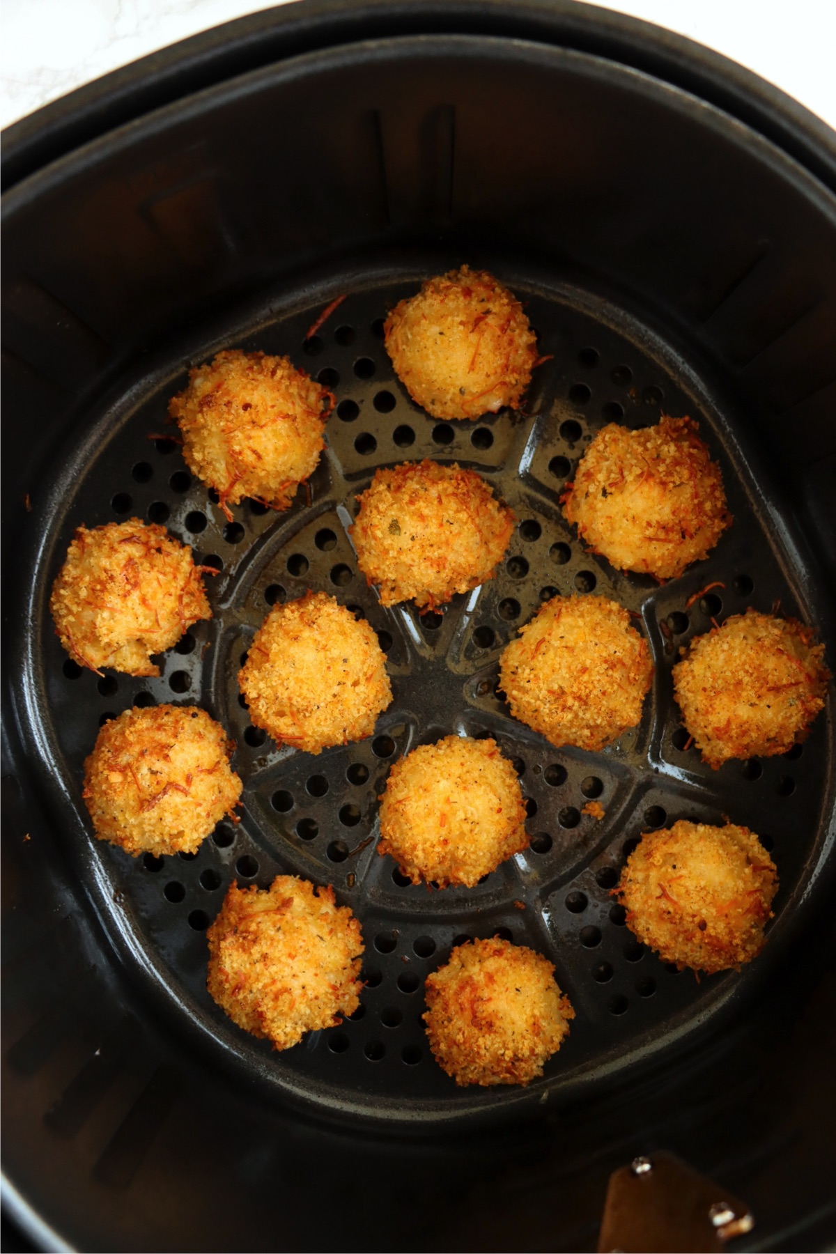 Mac and cheese bite appetizer air fried to a golden brown in an air fryer basket.