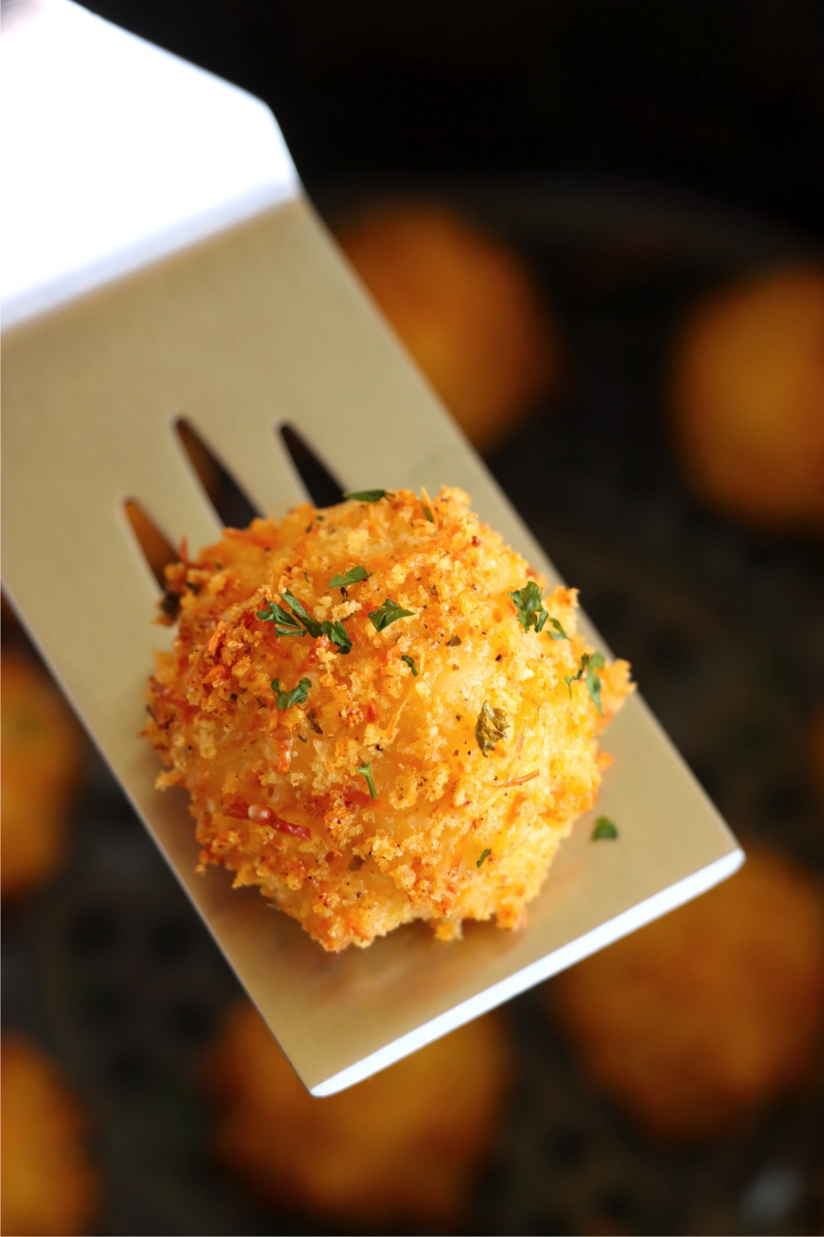 Metal spatula holding out a breaded mac and cheese bite.