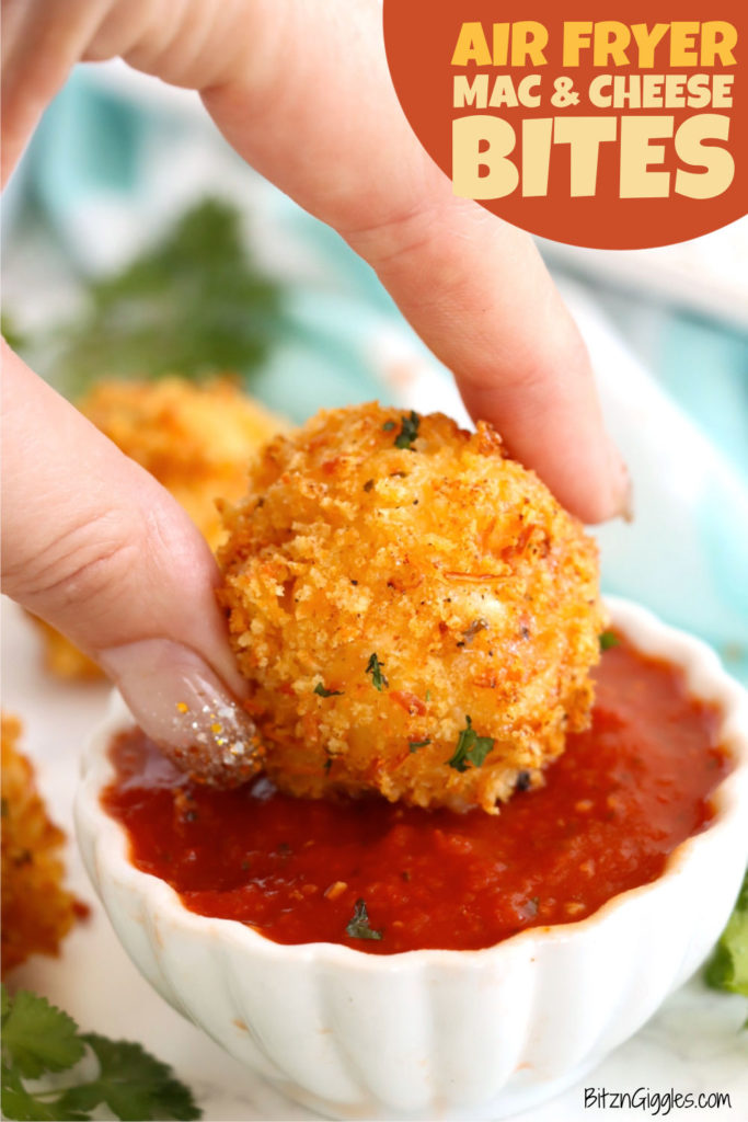 Fingers dipping a golden mac and cheese bite into a small bowl of marinara sauce.