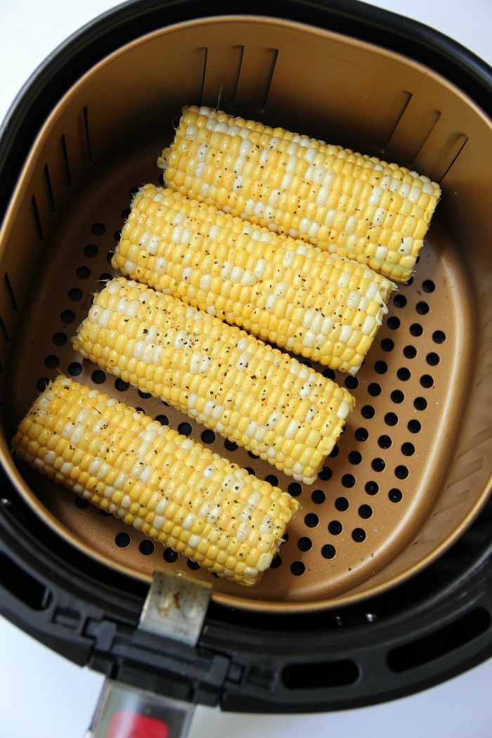 Raw corn on the cob in air fryer basket sprinkled with black pepper.