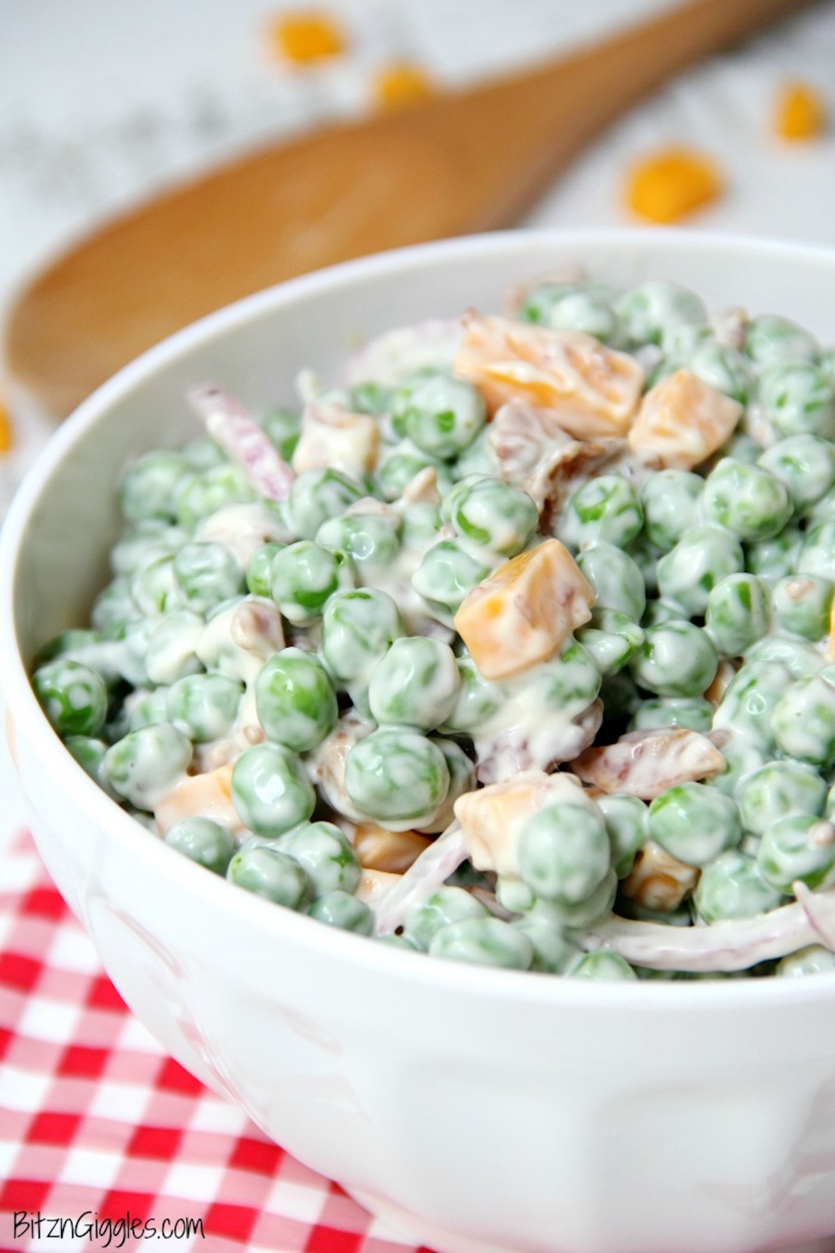 Pea salad in white serving bowl with wooden spoon.