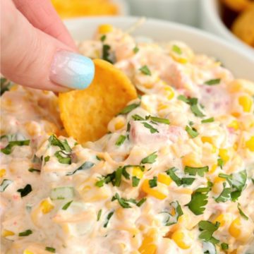 Frito dipping into Mexicorn dip in glass bowl.