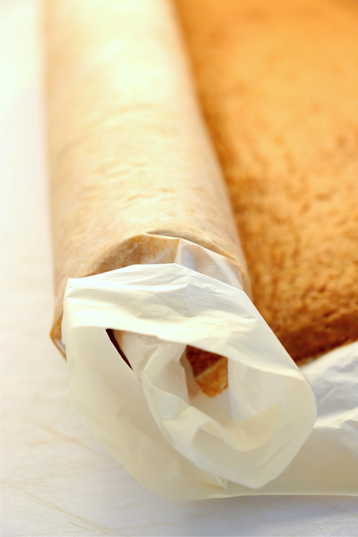 Rolling up a pumpkin cake in parchment paper.