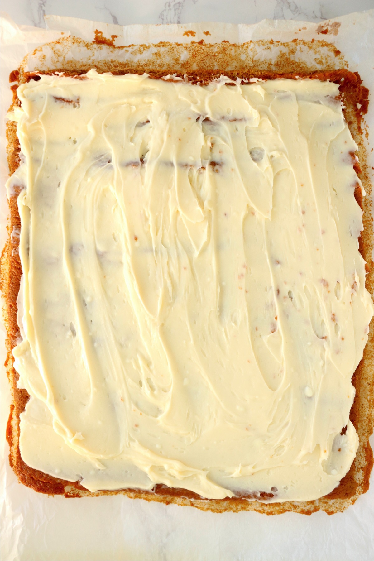 Cream cheese frosting spread over pumpkin cake baked in jelly roll pan.