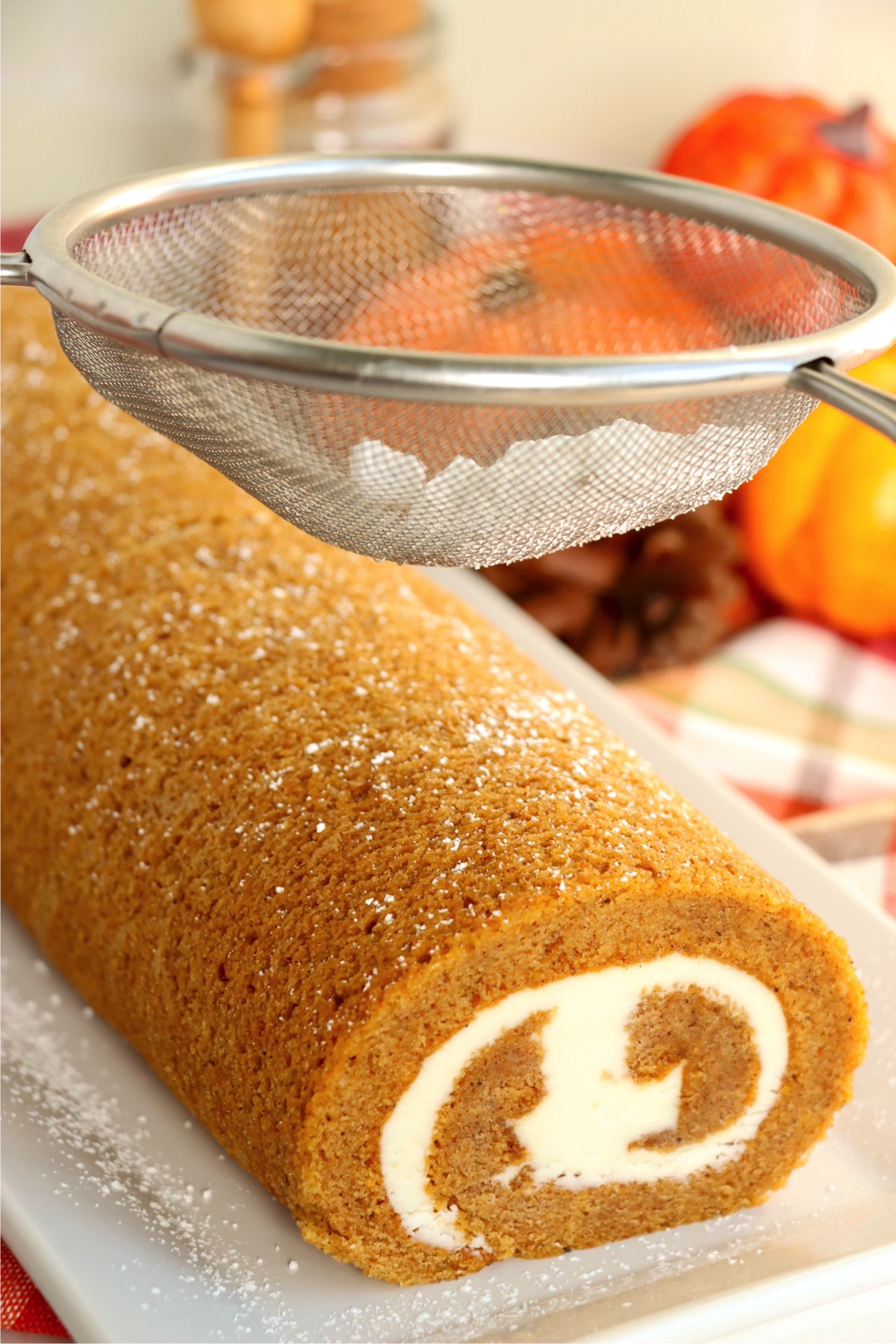 Sprinkling powdered sugar from a strainer onto a pumpkin cake roll.