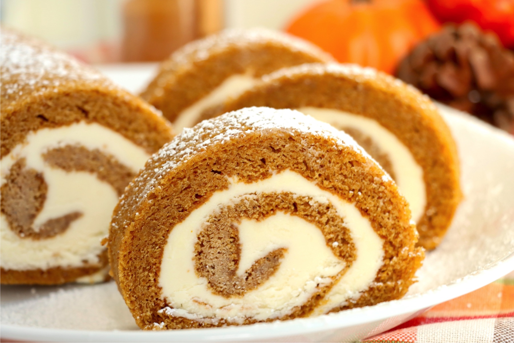 Four slices of a swirled pumpkin roll on a white serving plate.