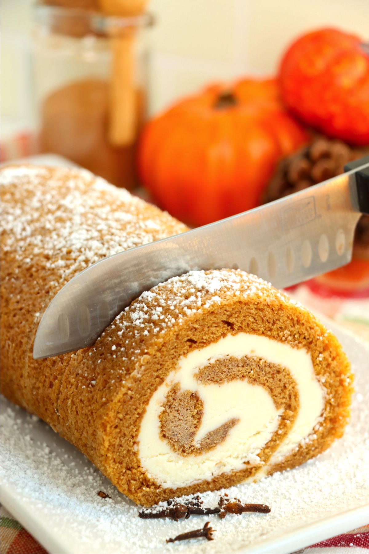 Knife cutting into a swirled pumpkin cheesecake roll.