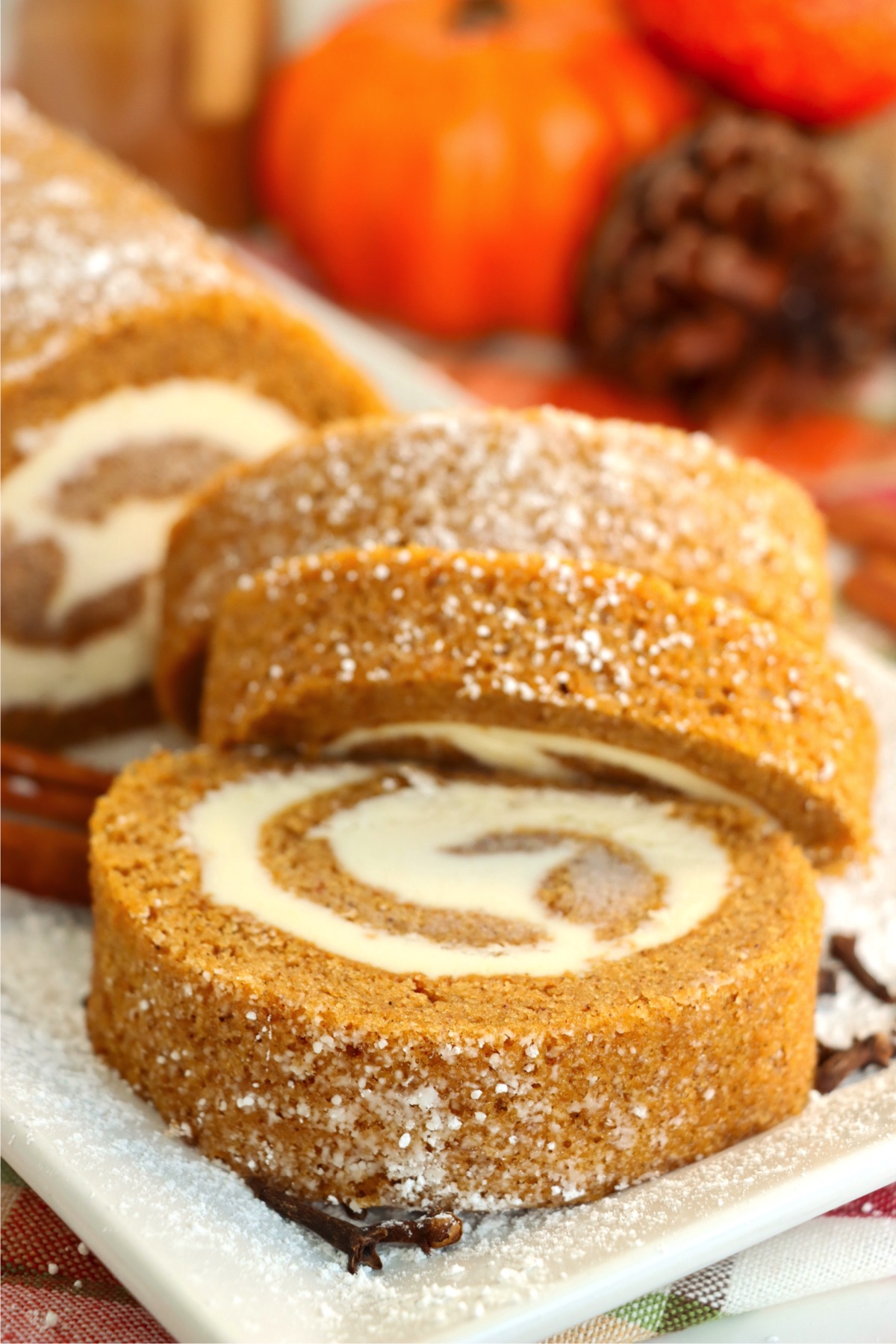 Three pieces of swirled pumpkin roll dessert displayed on a white plate with fall decorations in the background.