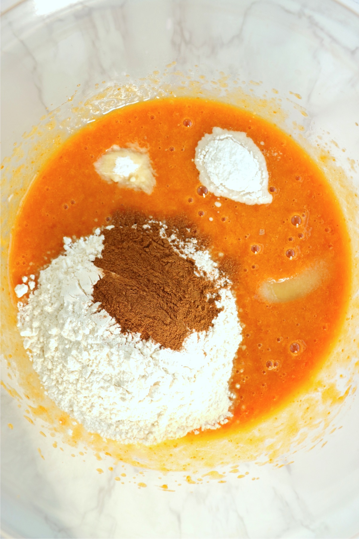 Flour, baking powder, baking soda and pumpkin pie spice added to a bowl of canned pumpkin.