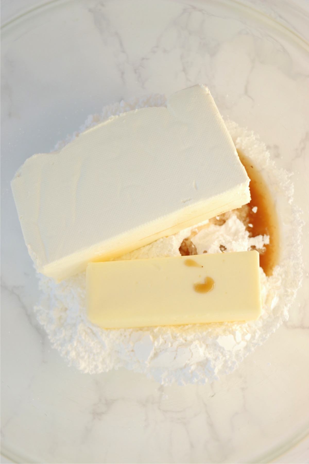 Cream cheese, powdered sugar, butter and vanilla extract in a glass mixing bowl.