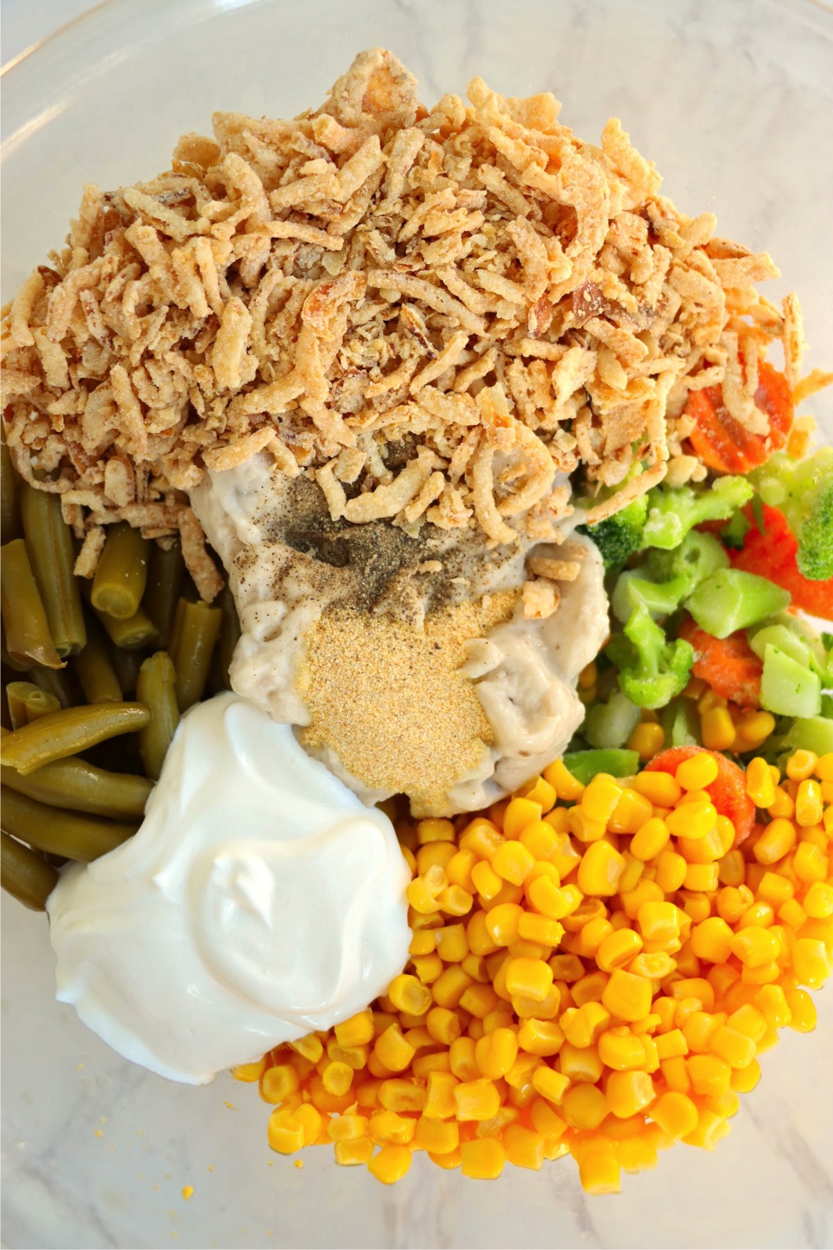 A mixing bowl filled with vegetables, cream of mushroom soup, sour cream, crispy onions and seasonings.