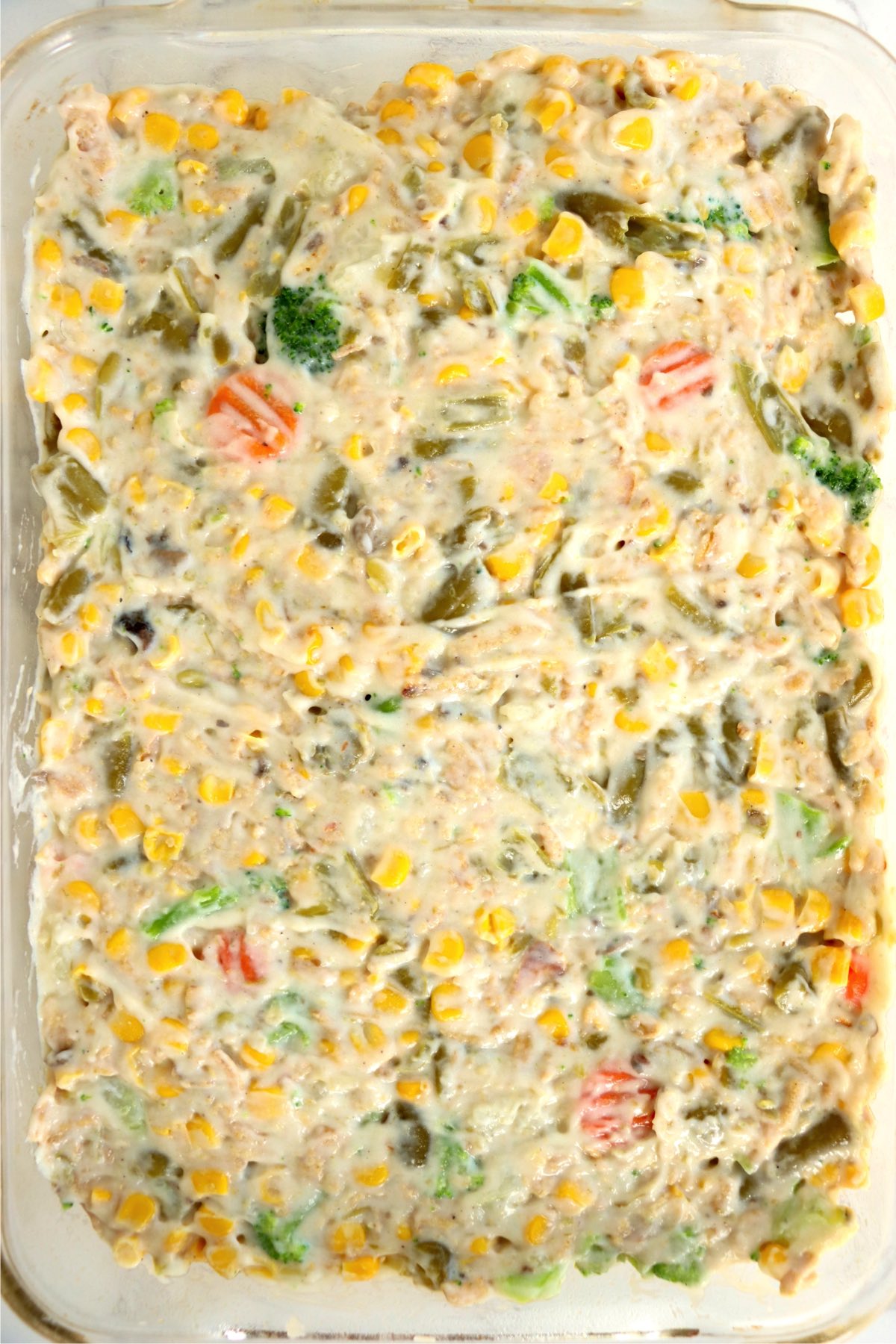 Baking pan filled with mixed vegetables covered in a creamy sauce.