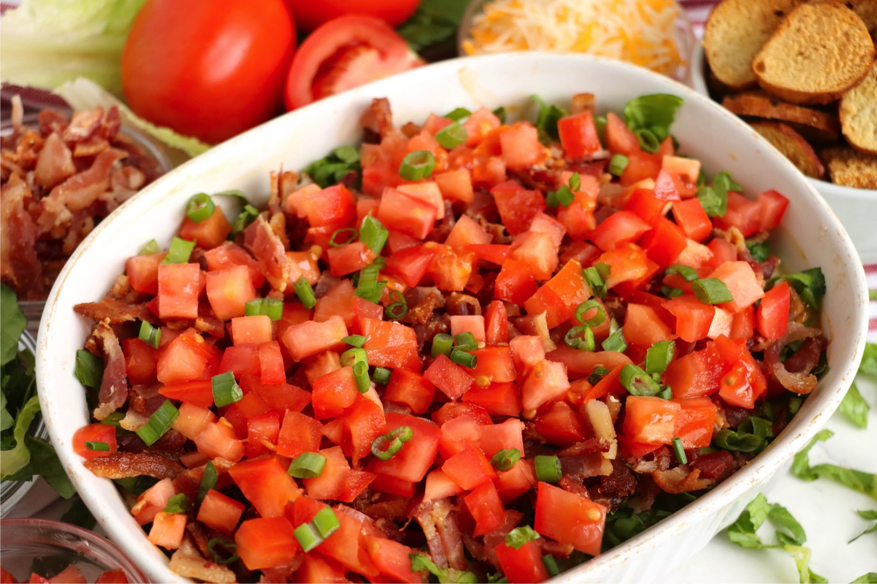 Hot BLT dip in a white dish, layered with bacon, lettuce, and tomatoes.