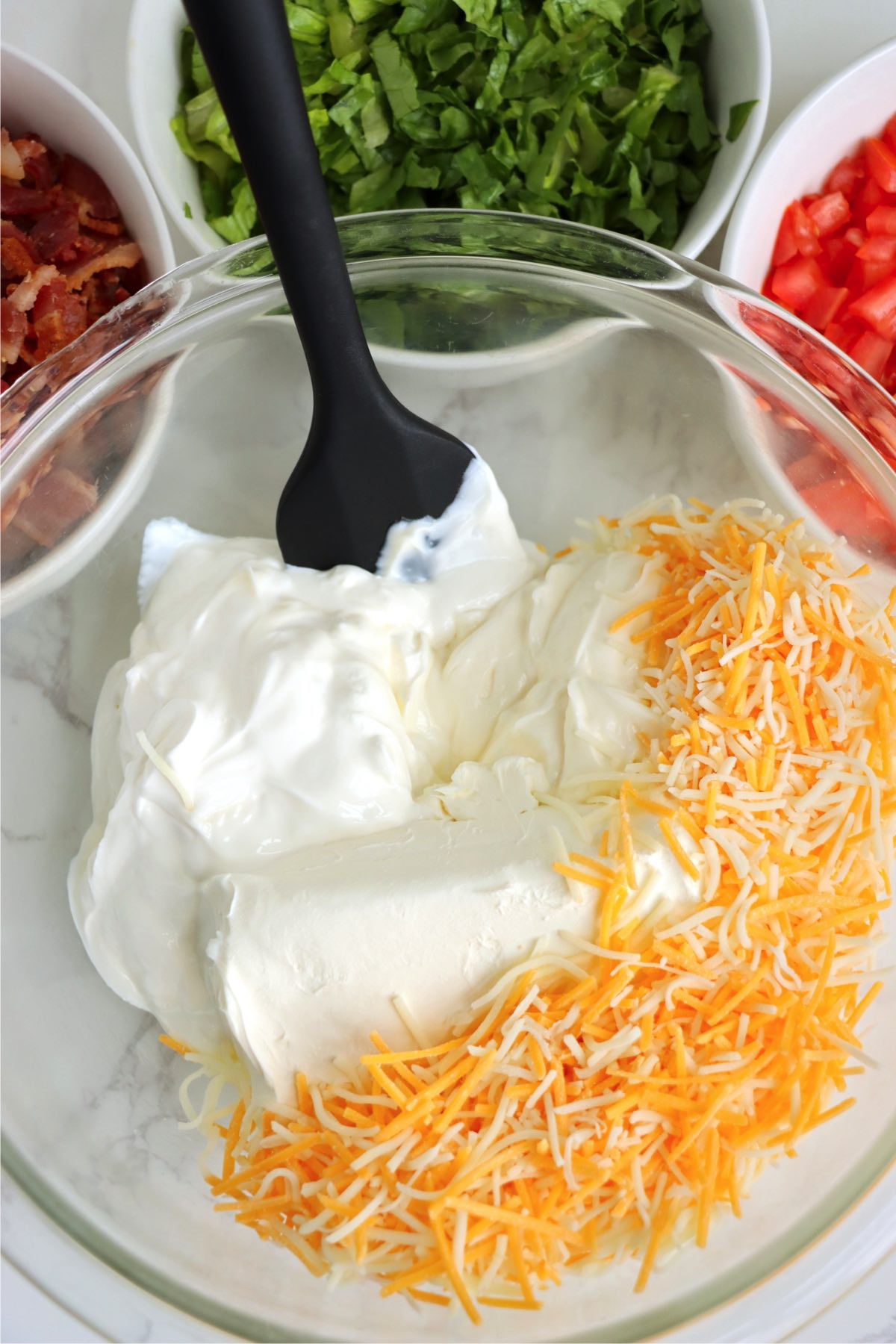 Mixing together cheese, sour cream and cream cheese in a glass bowl