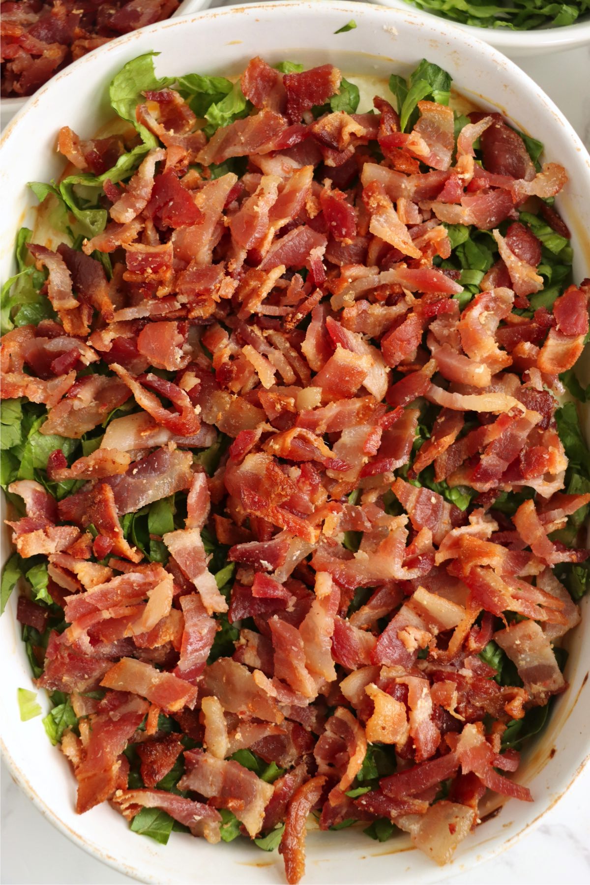 White baking dish filled with BLT dip that's topped with lettuce and bacon.