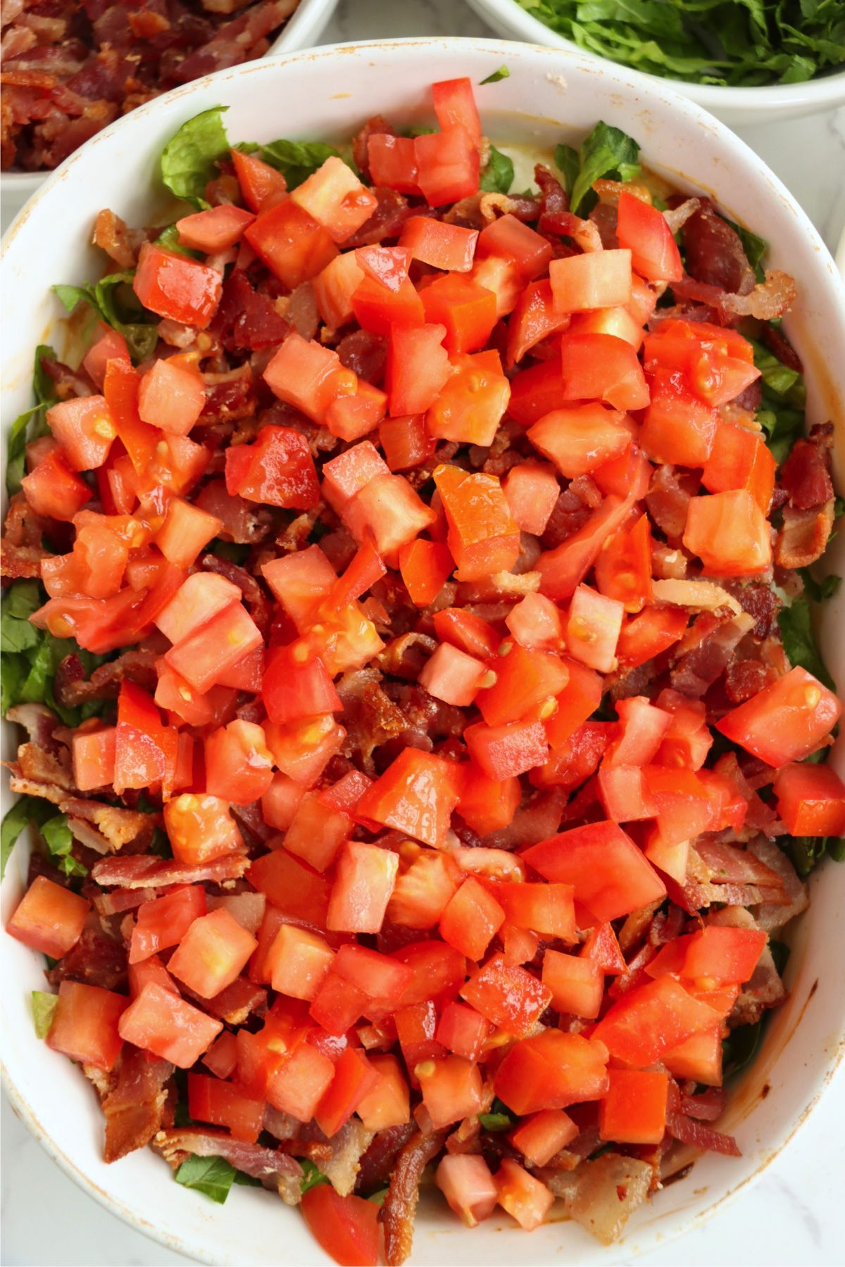 Baked BLT dip topped with lettuce and tomatoes in a white baking dish.