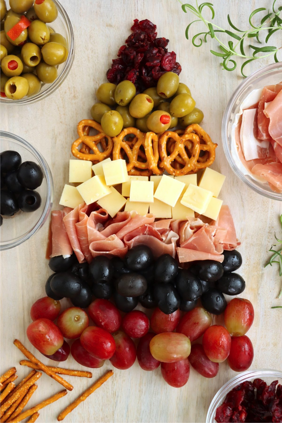 Step-by-step assembly of a charcuterie Christmas tree, layering meats, cheeses, fruits, and vegetables into a festive holiday design before adding the final touches.