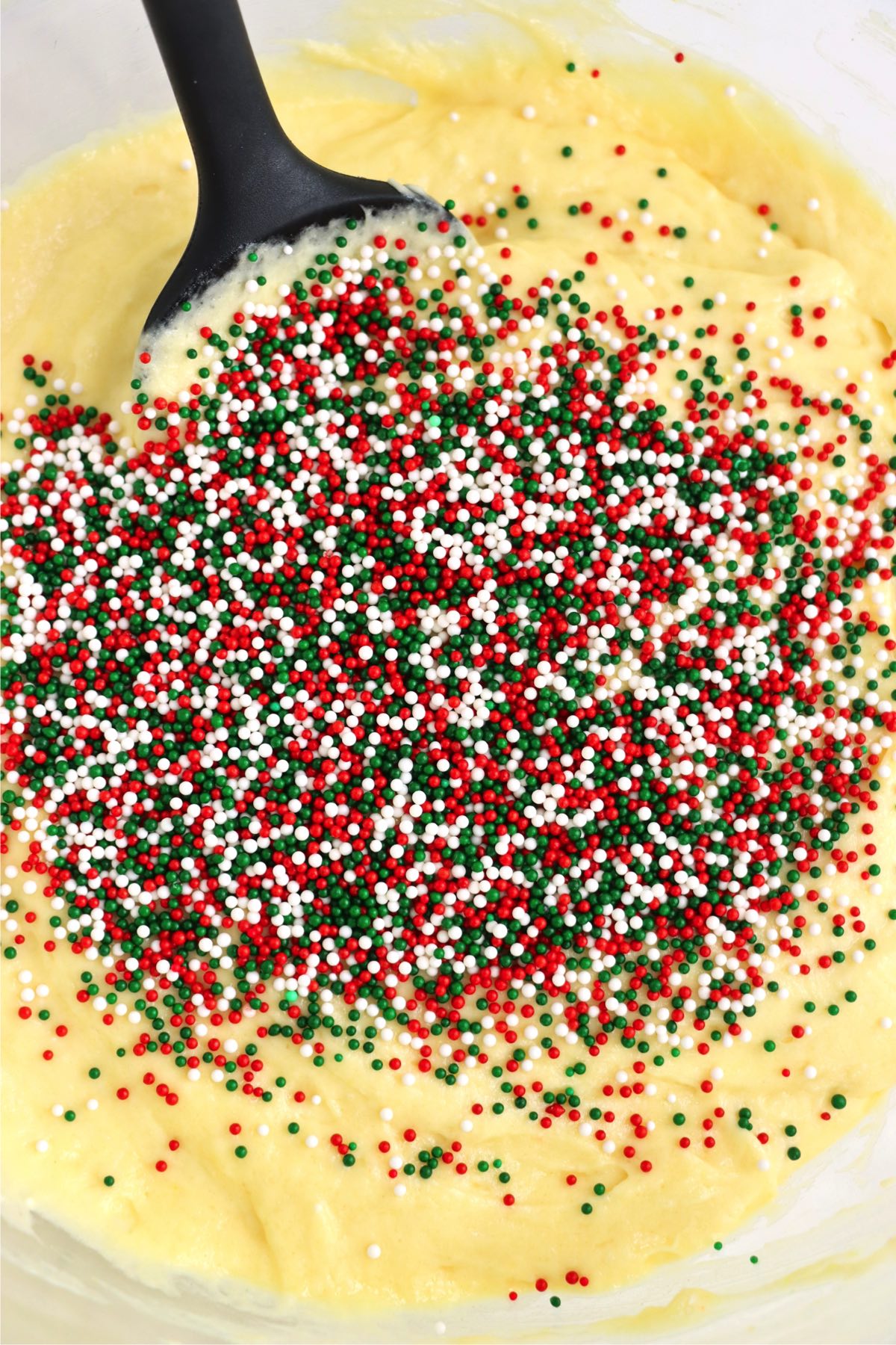 Red and green sprinkles in a bowl with cake batter.