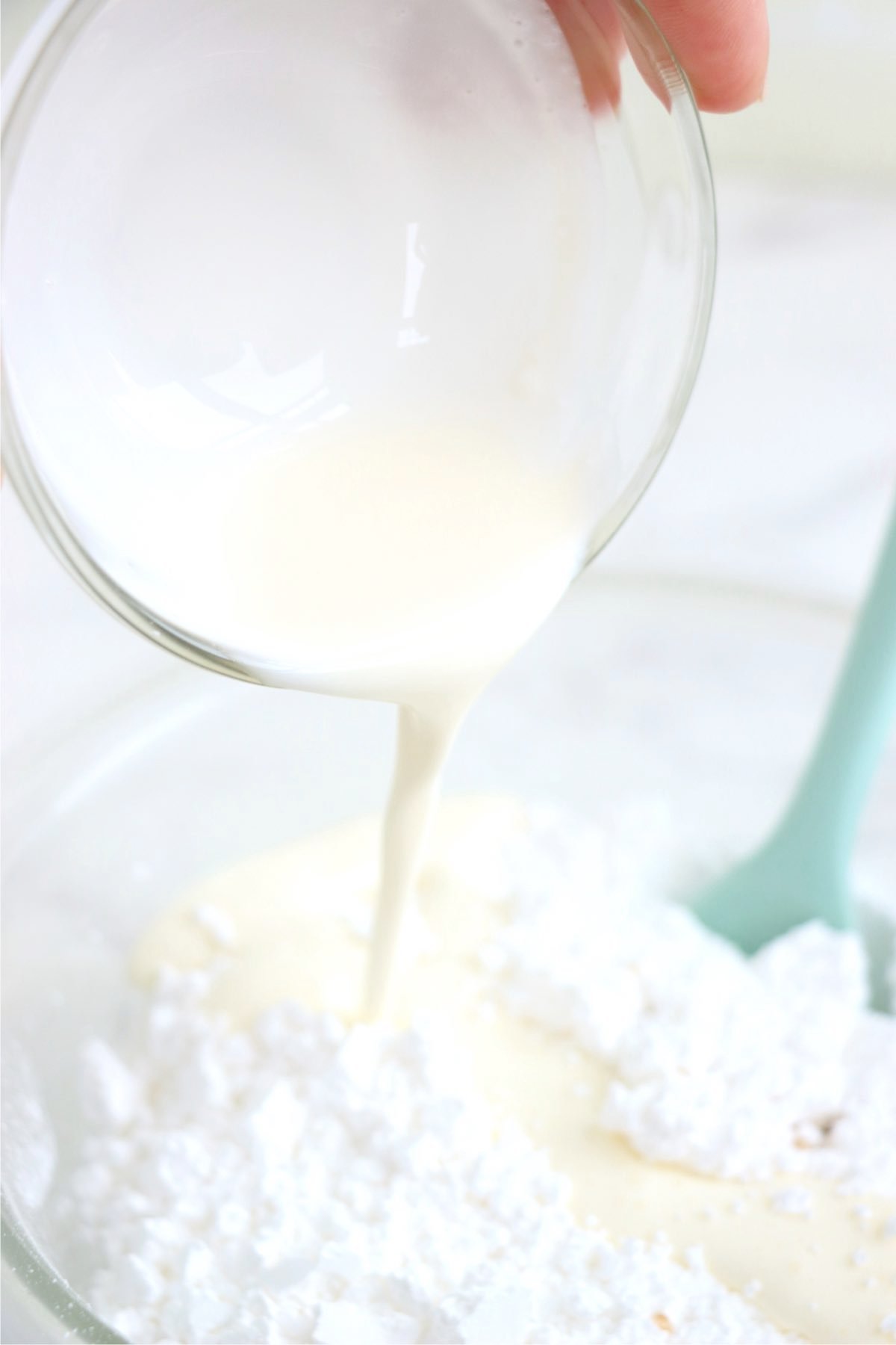 Pouring heavy whipping cream out of a measuring cup into a bowl of powdered sugar.