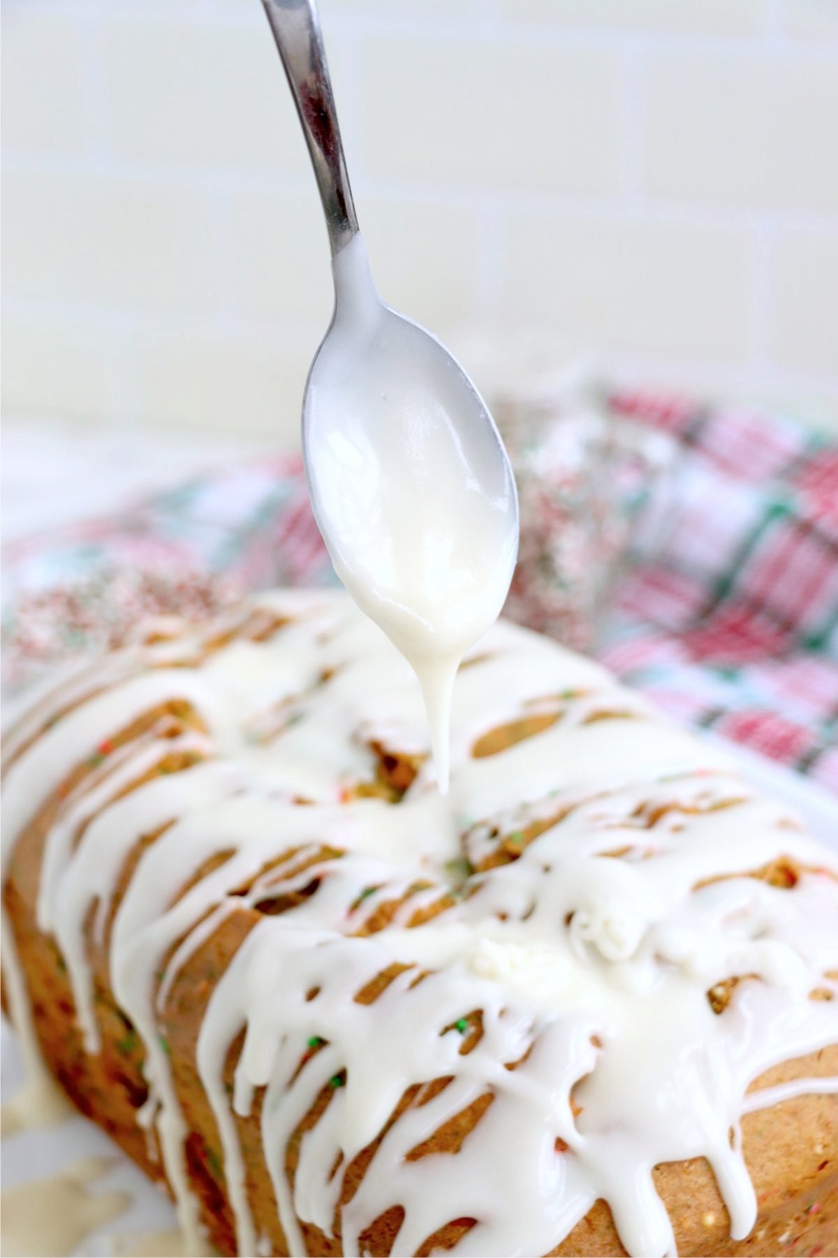 Spoon drizzling icing over the top of a loaf of sweet Christmas bread.