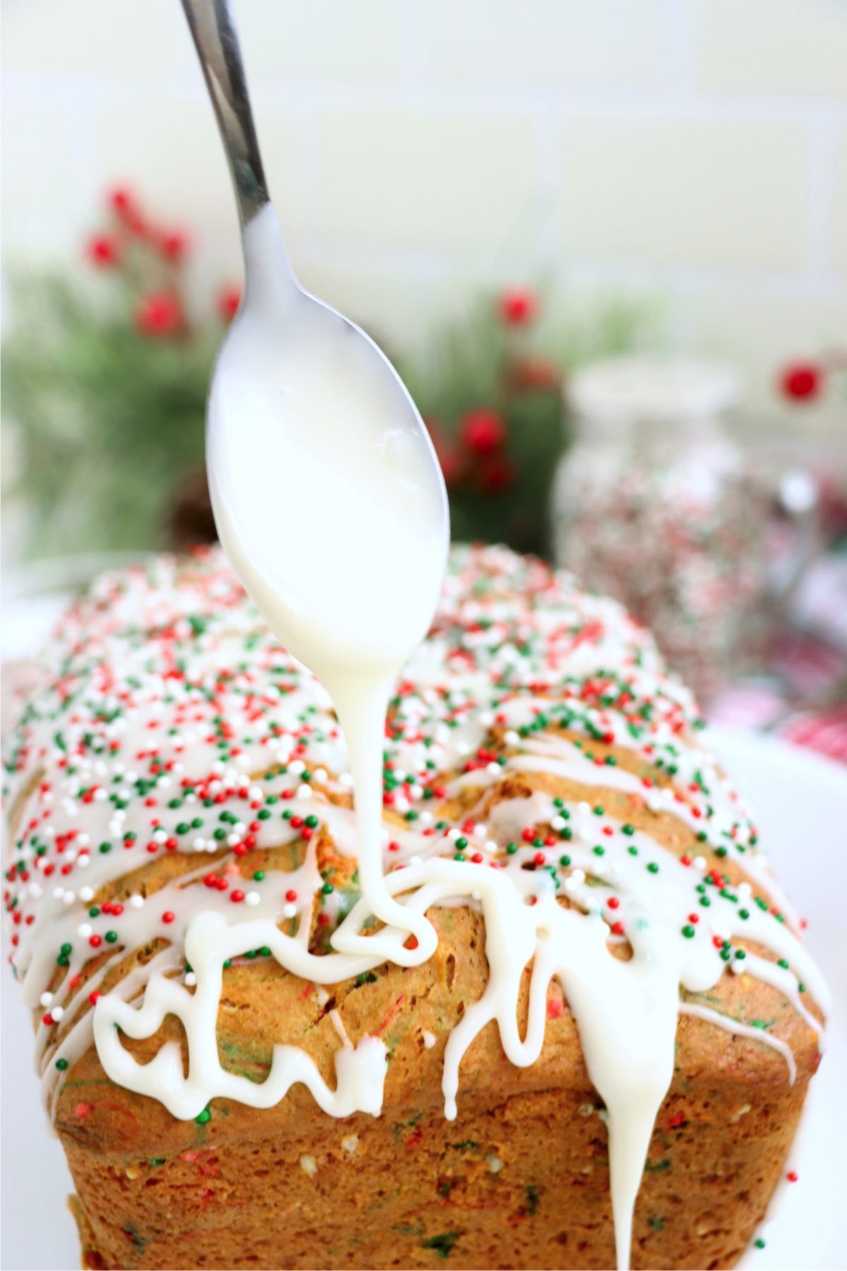 Spoon drizzling icing over the top of a loaf of Christmas bread.