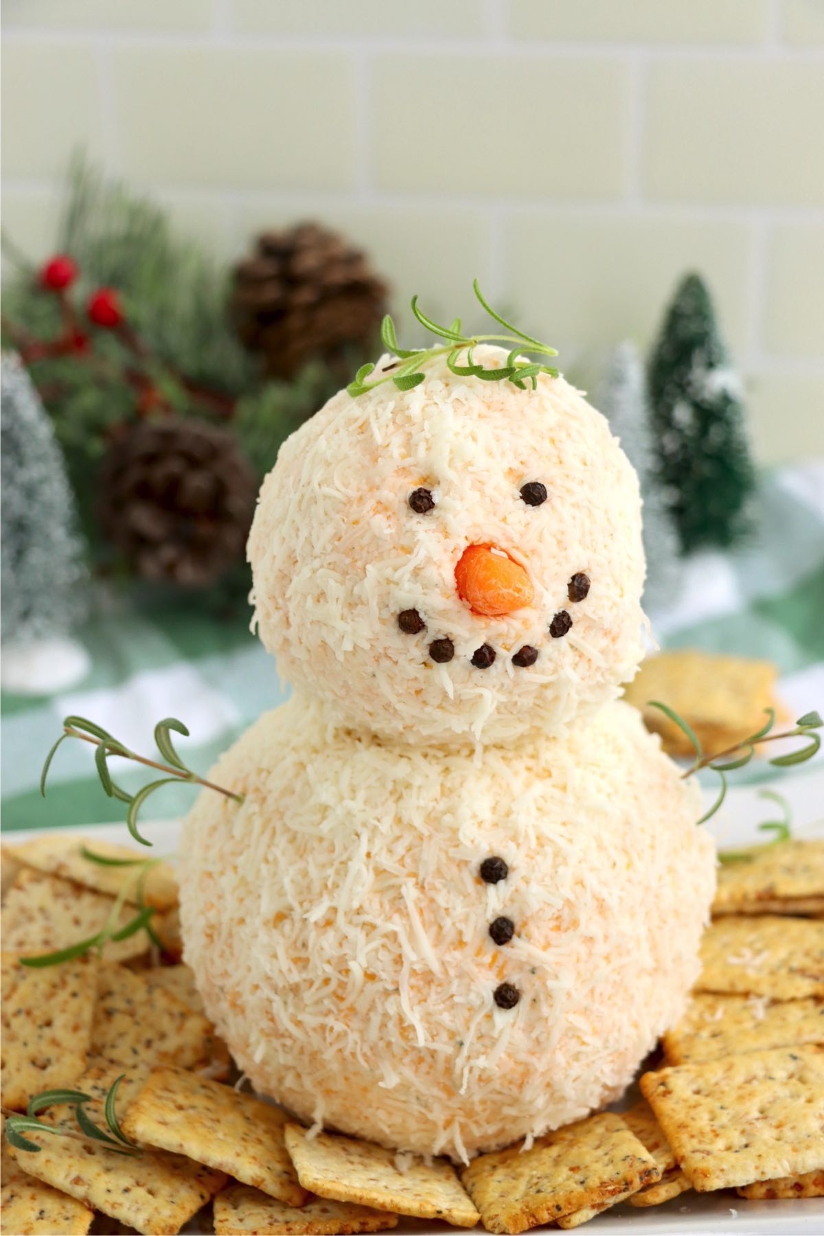 Snowman cheeseball with rosemary sprigs for arms surrounded by crackers.