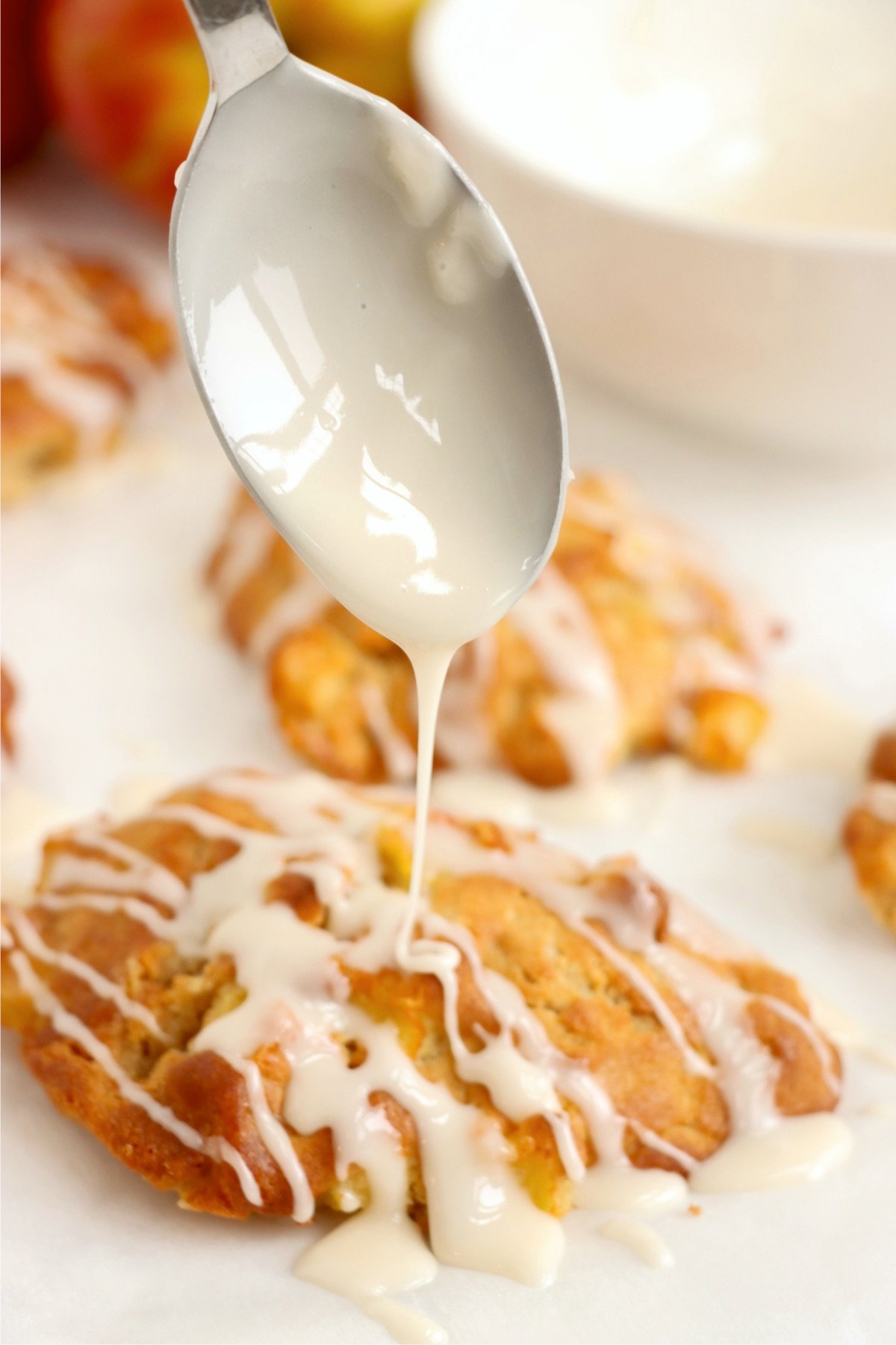 Using a spoon to drizzle icing over apple fritters made in the air fryer.