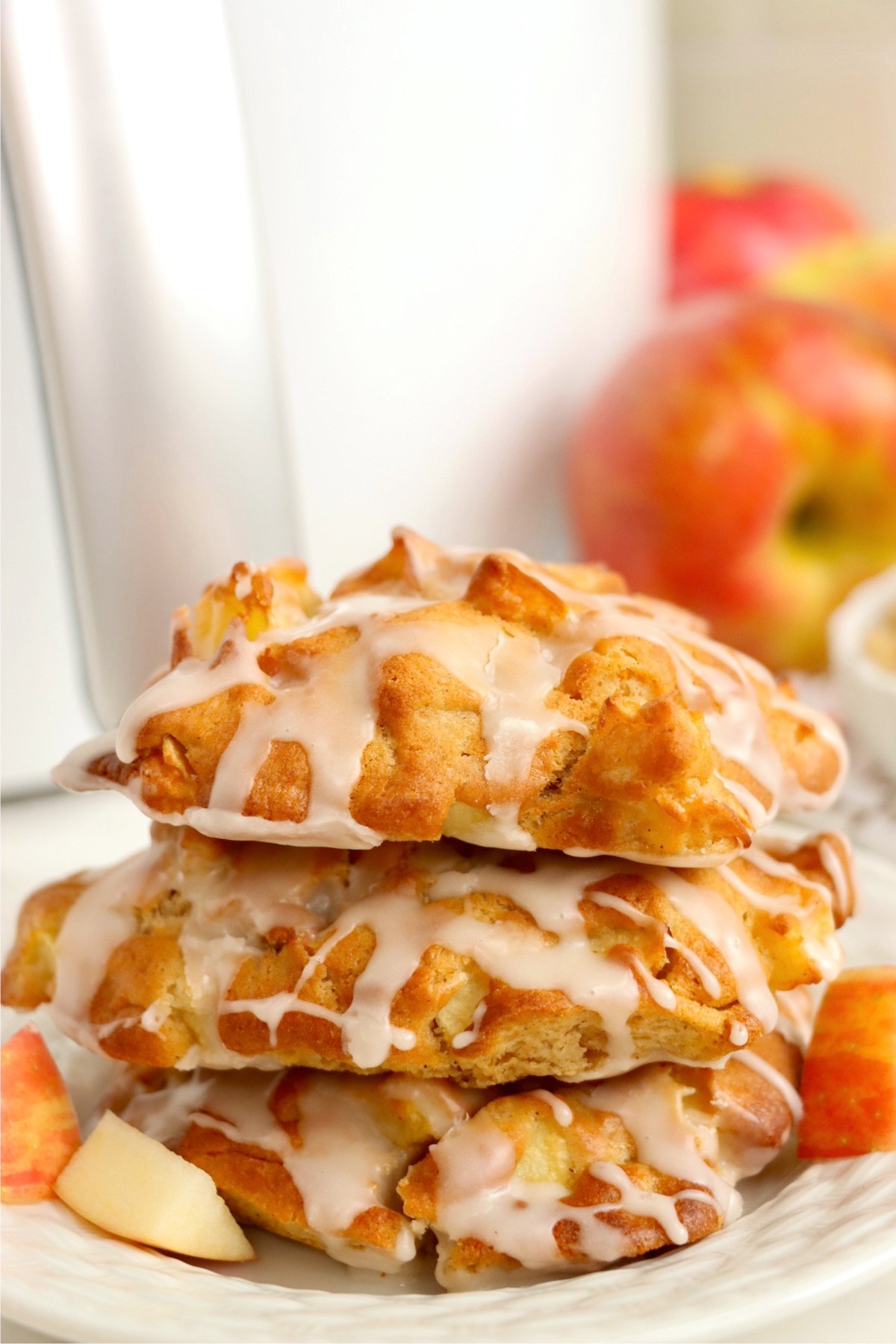 A stack of three apple fritters on a white plate in front of an air fryer.