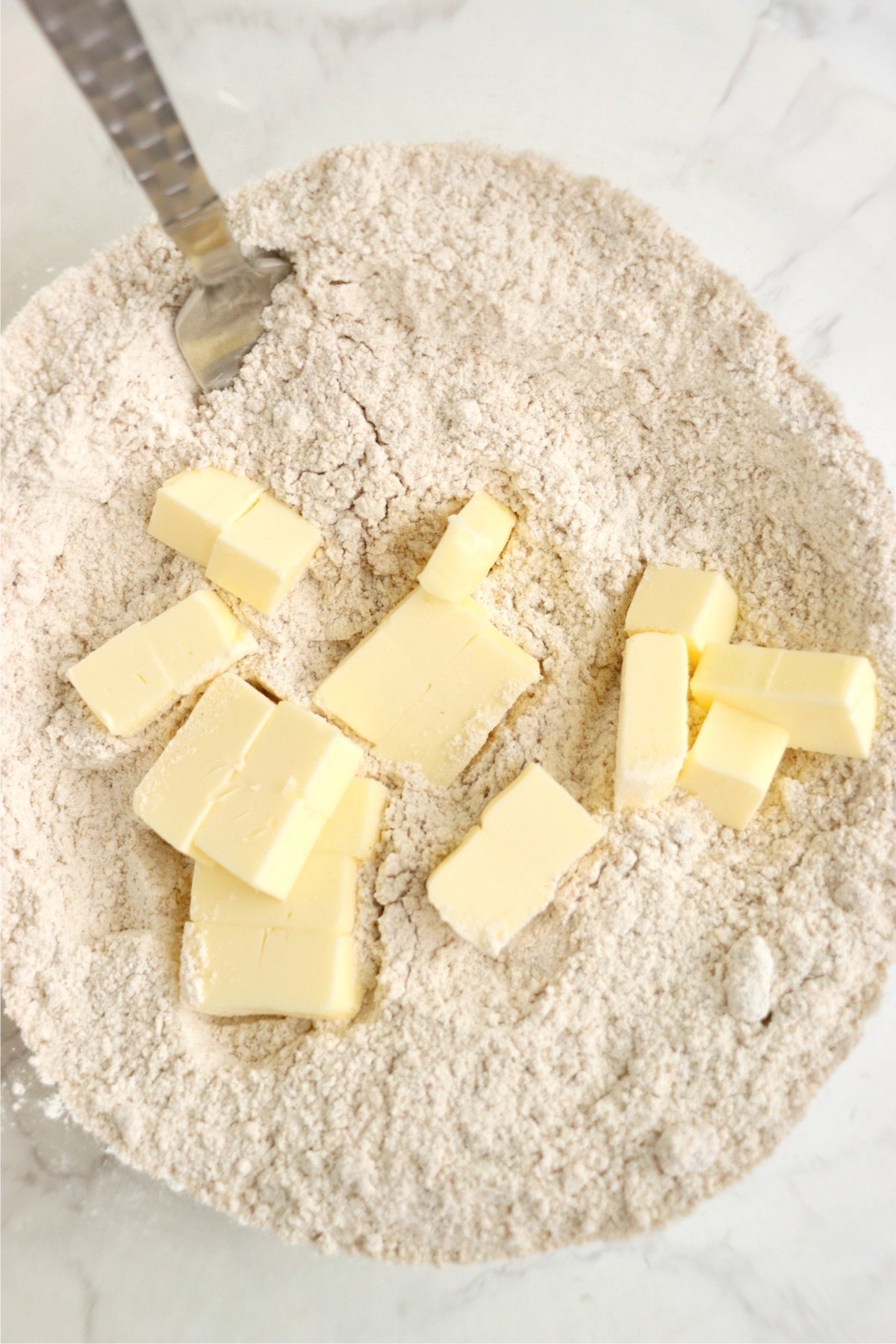 Cold cubed butter being added to the dry ingredients, ready to be incorporated for the perfect apple fritters batter.