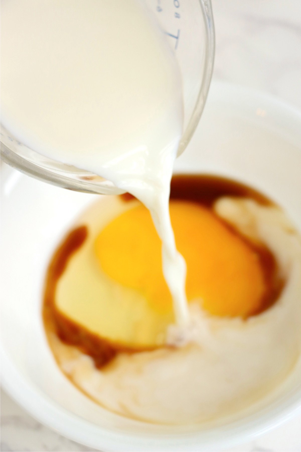 Milk being poured into a bowl of wet ingredients, including an egg and vanilla extract, for an air fryer apple fritters recipe.