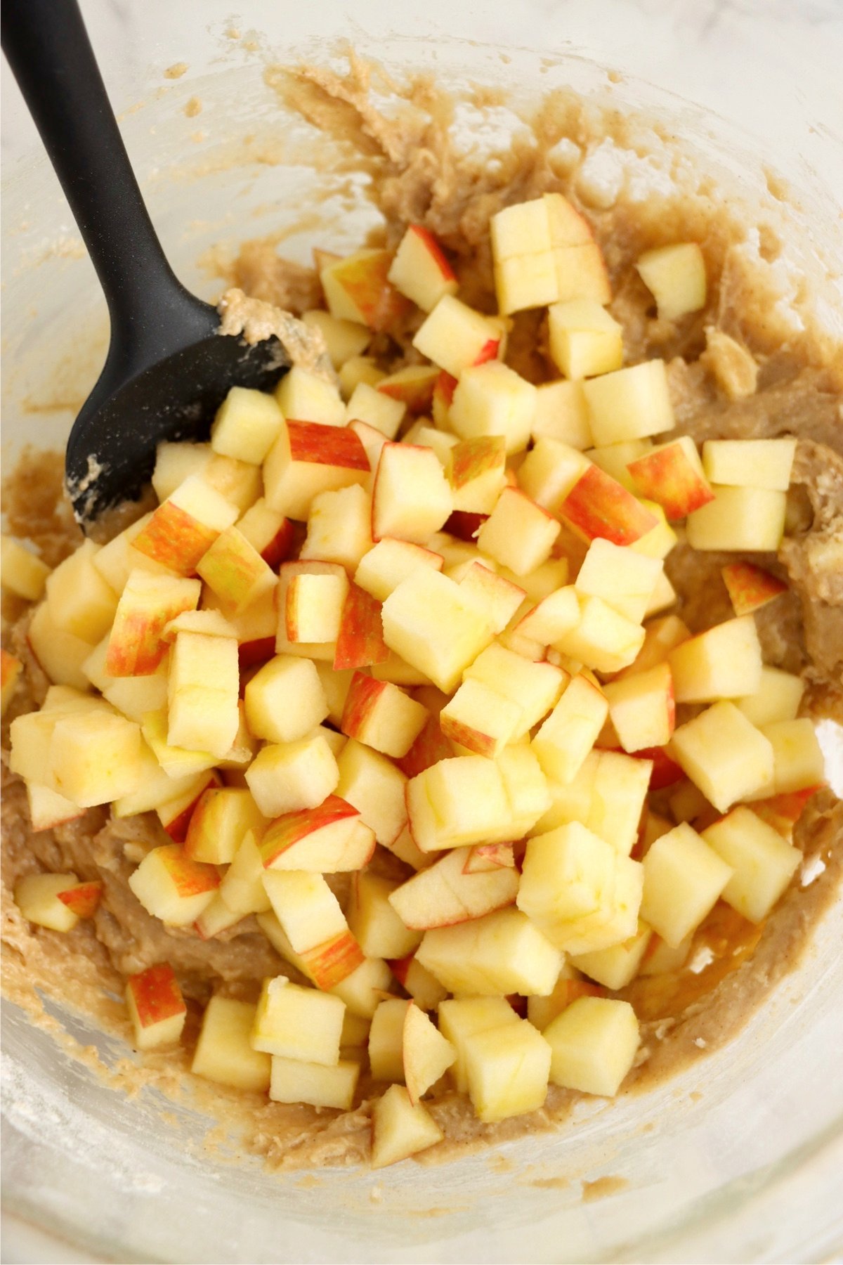 Freshly chopped apples being mixed into the batter of air fryer apple fritters.