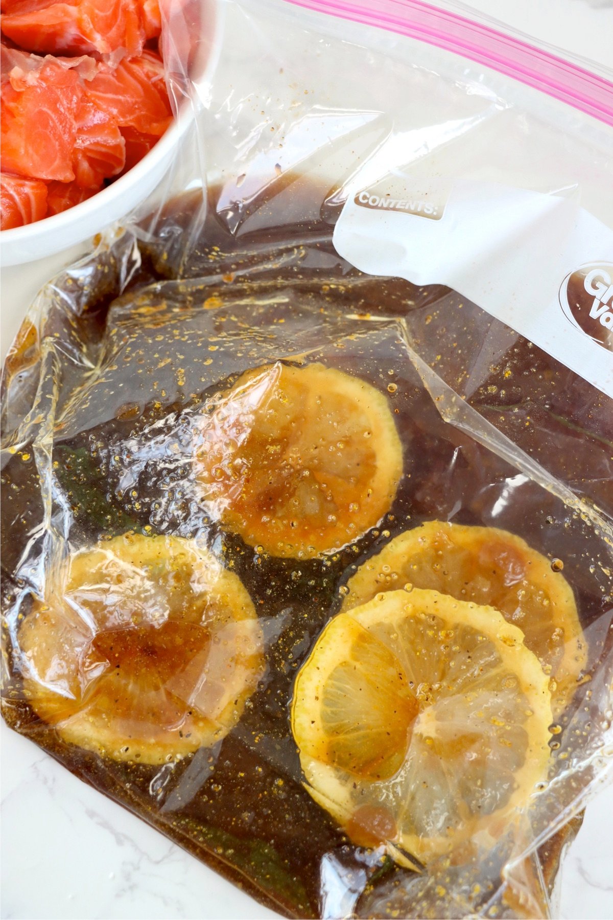 Fresh lemon slices added to a ziplock bag filled with a sweet and savory salmon marinade.