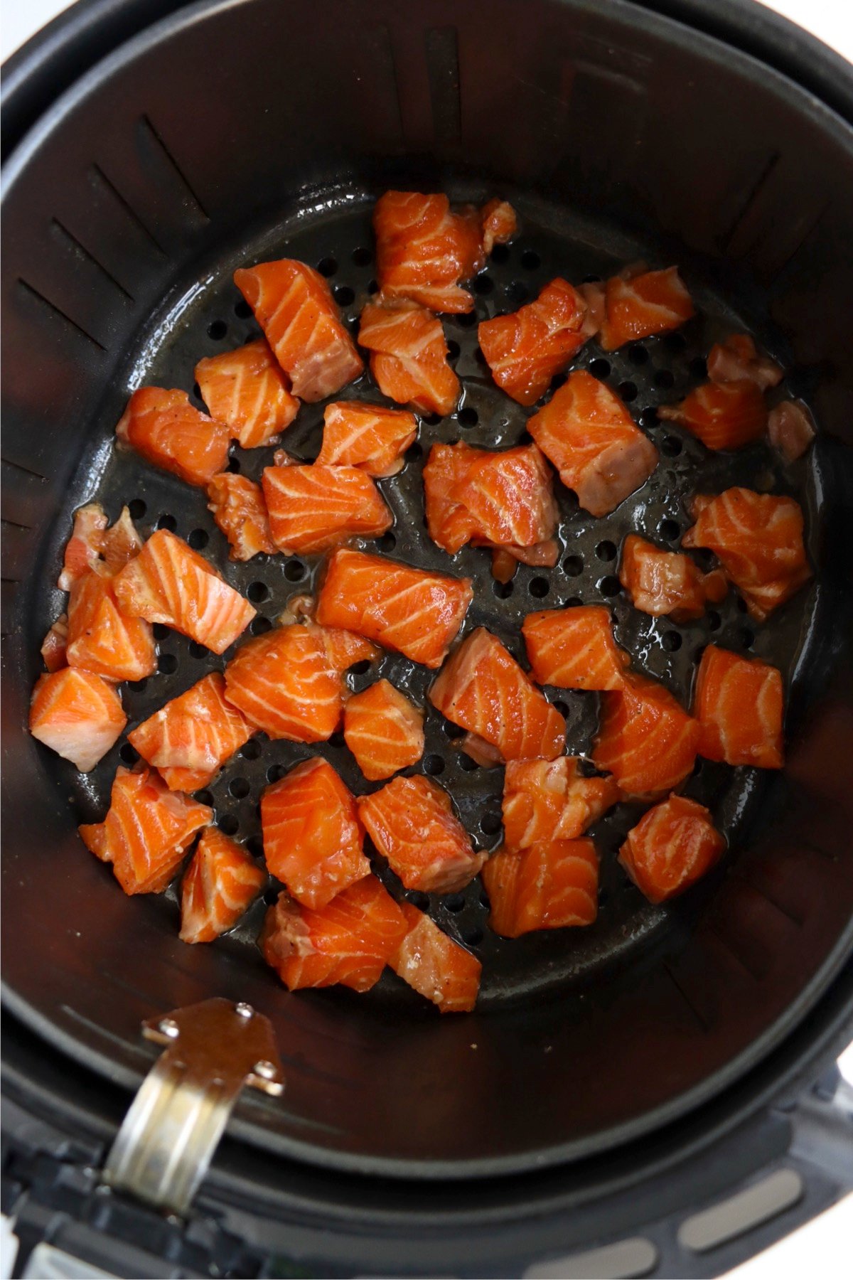 Marinated salmon bites arranged evenly in the air fryer basket, ready to cook to perfection.