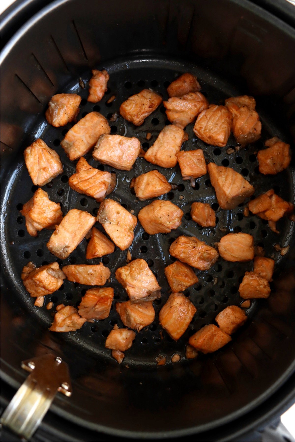 Cooked salmon bites in an air fryer basket.