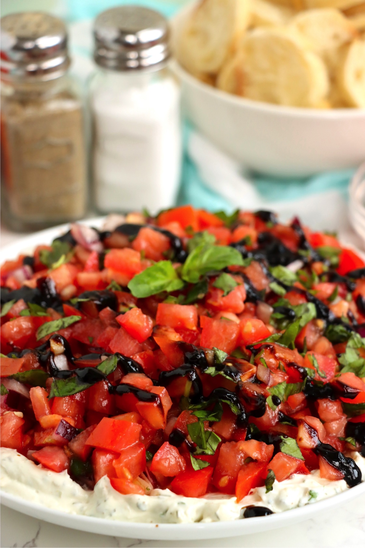 Close-up of bruschetta dip with a creamy white cheese base, vibrant diced tomatoes, fresh basil, and a glossy drizzle of dark balsamic glaze on top