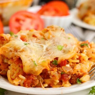 A single serving of lasagna casserole on a white plate, featuring layered pasta, meat sauce, and cheese, with fresh parsley and tomato slices nearby.