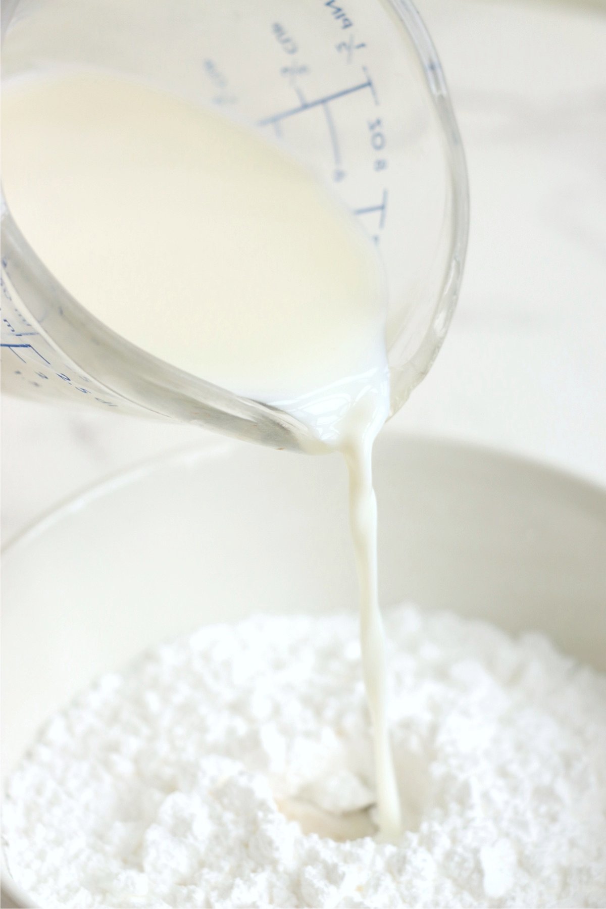 Pouring milk into powdered sugar to create icing for apple fritters.