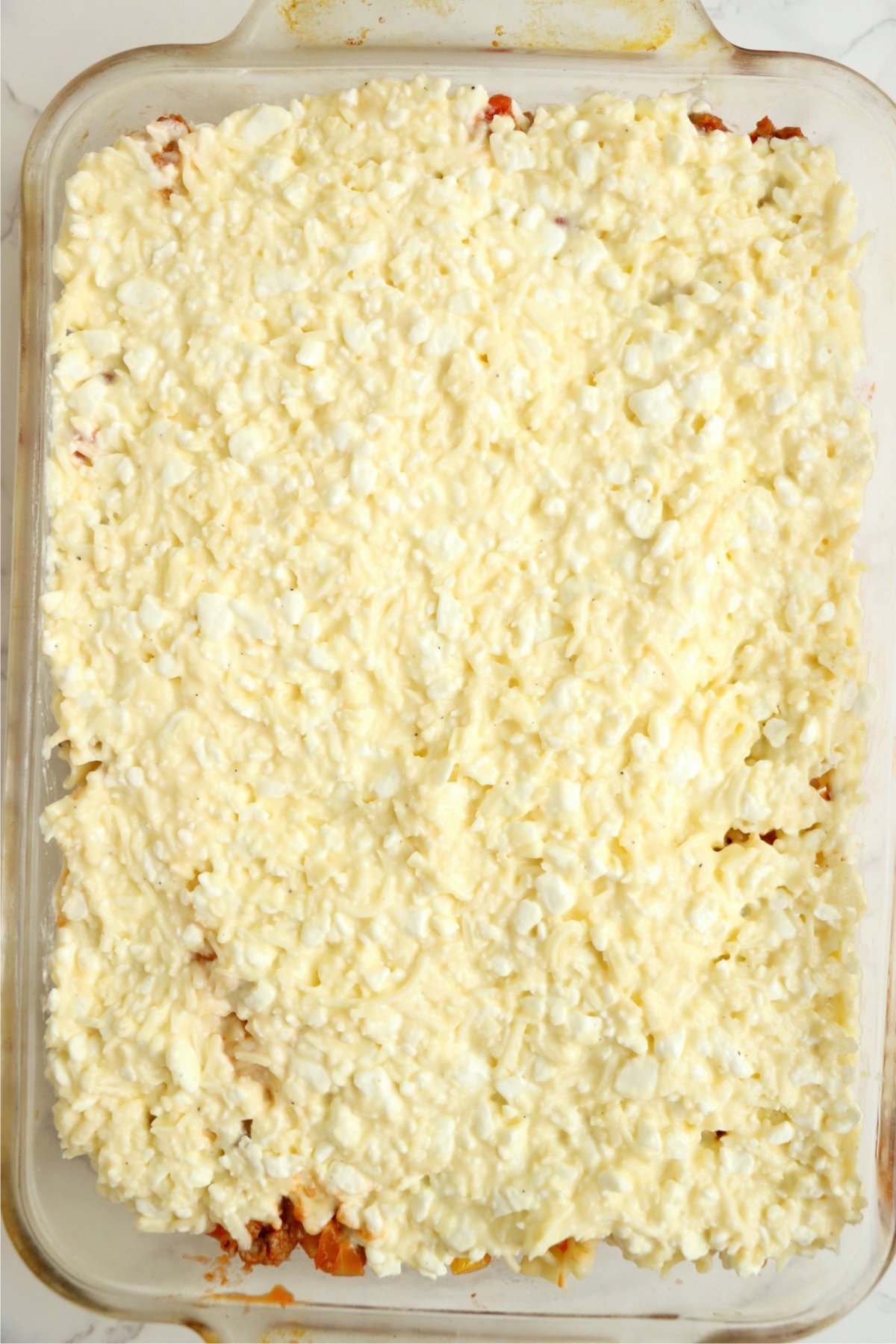 Casserole dish is layered with a creamy cheese mixture, spread evenly over the pasta and meat sauce.