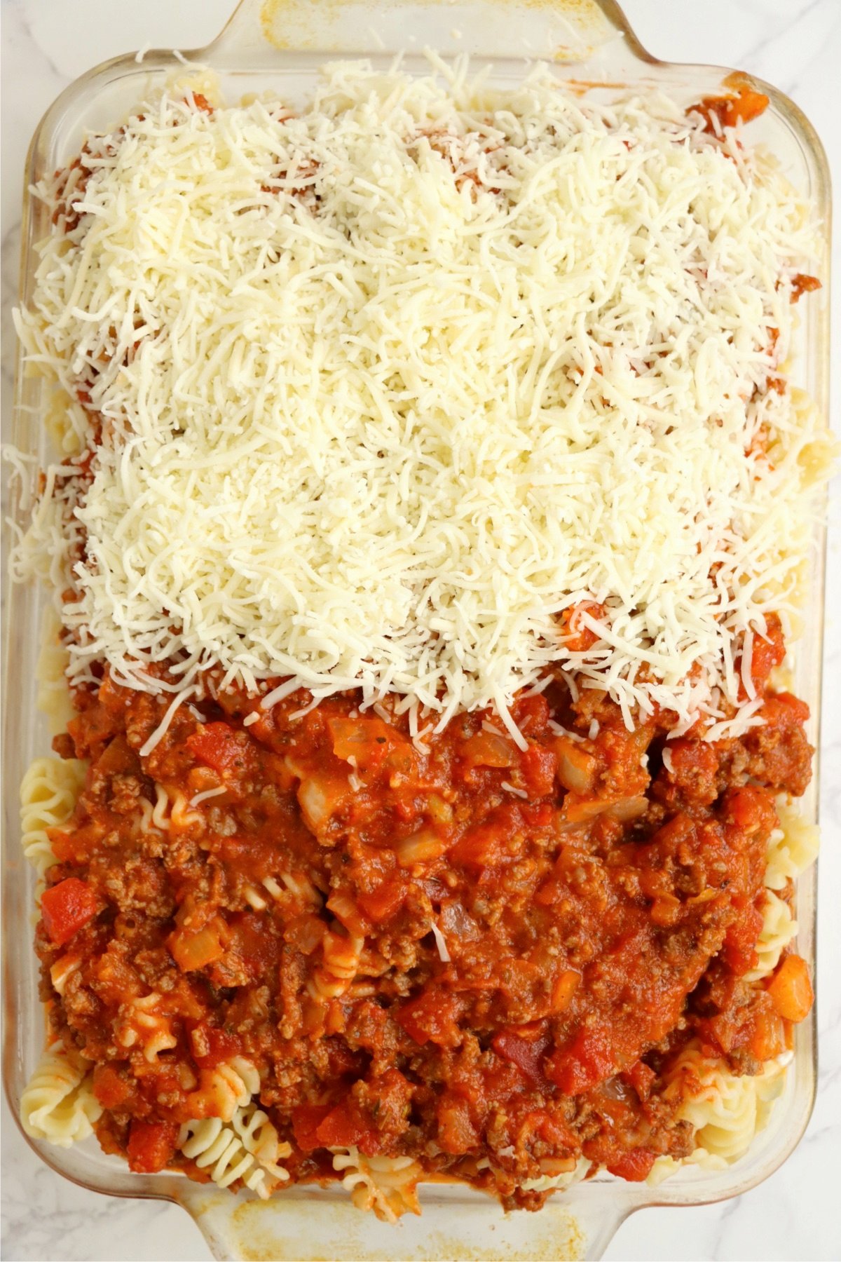 A creamy cheese mixture, spread evenly over the pasta and meat sauce in a casserole dish.