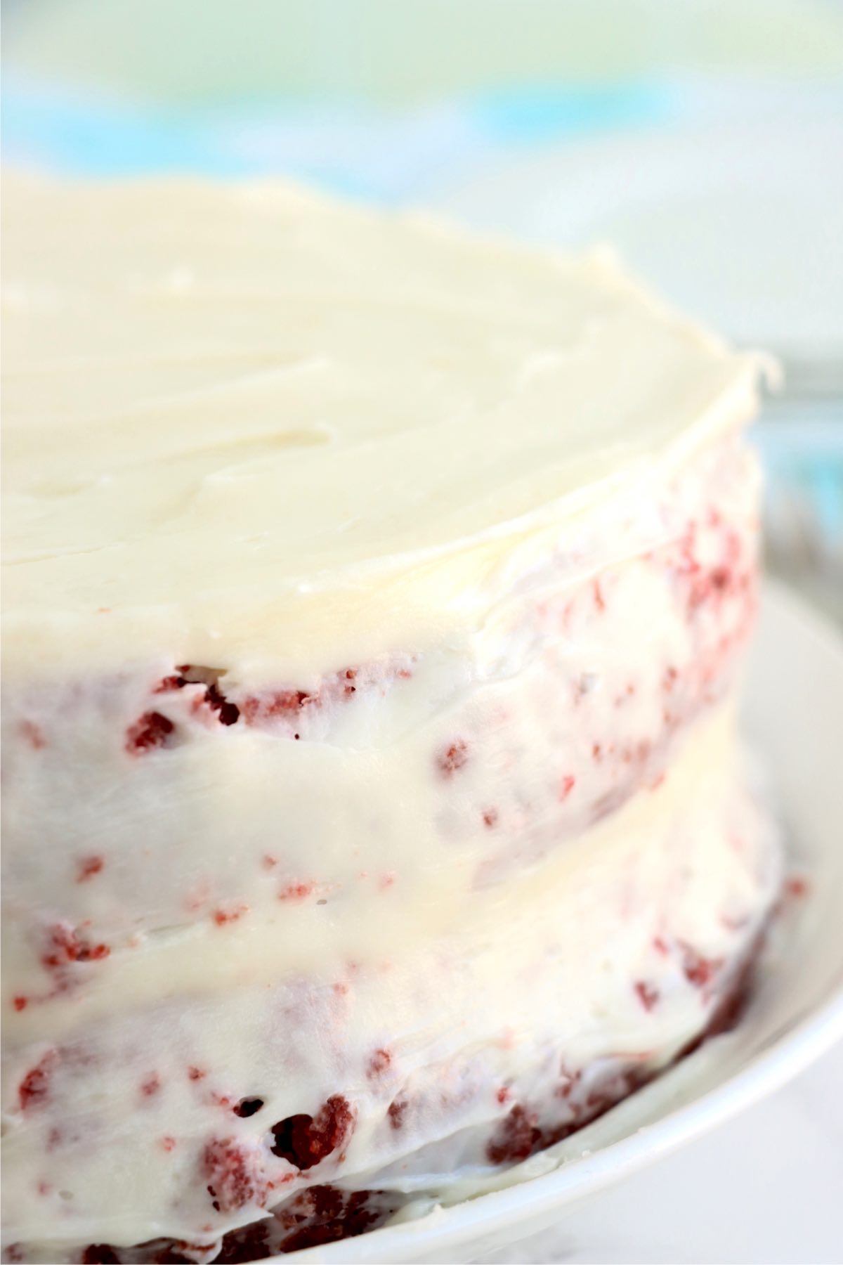 A lightly iced red velvet layer cake on a serving plate.